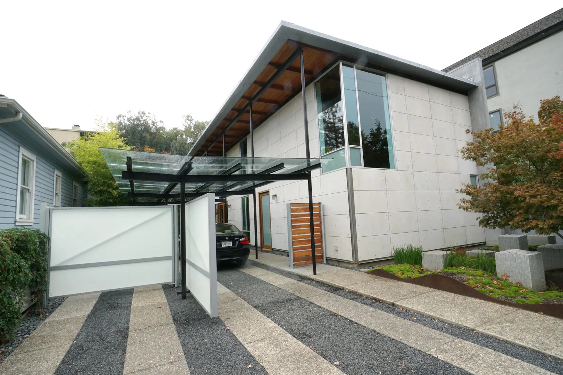 Modern residential home with white exterior, angled roof, glass entry, striped concrete driveway, and integrated garage by Leibin Architecture.