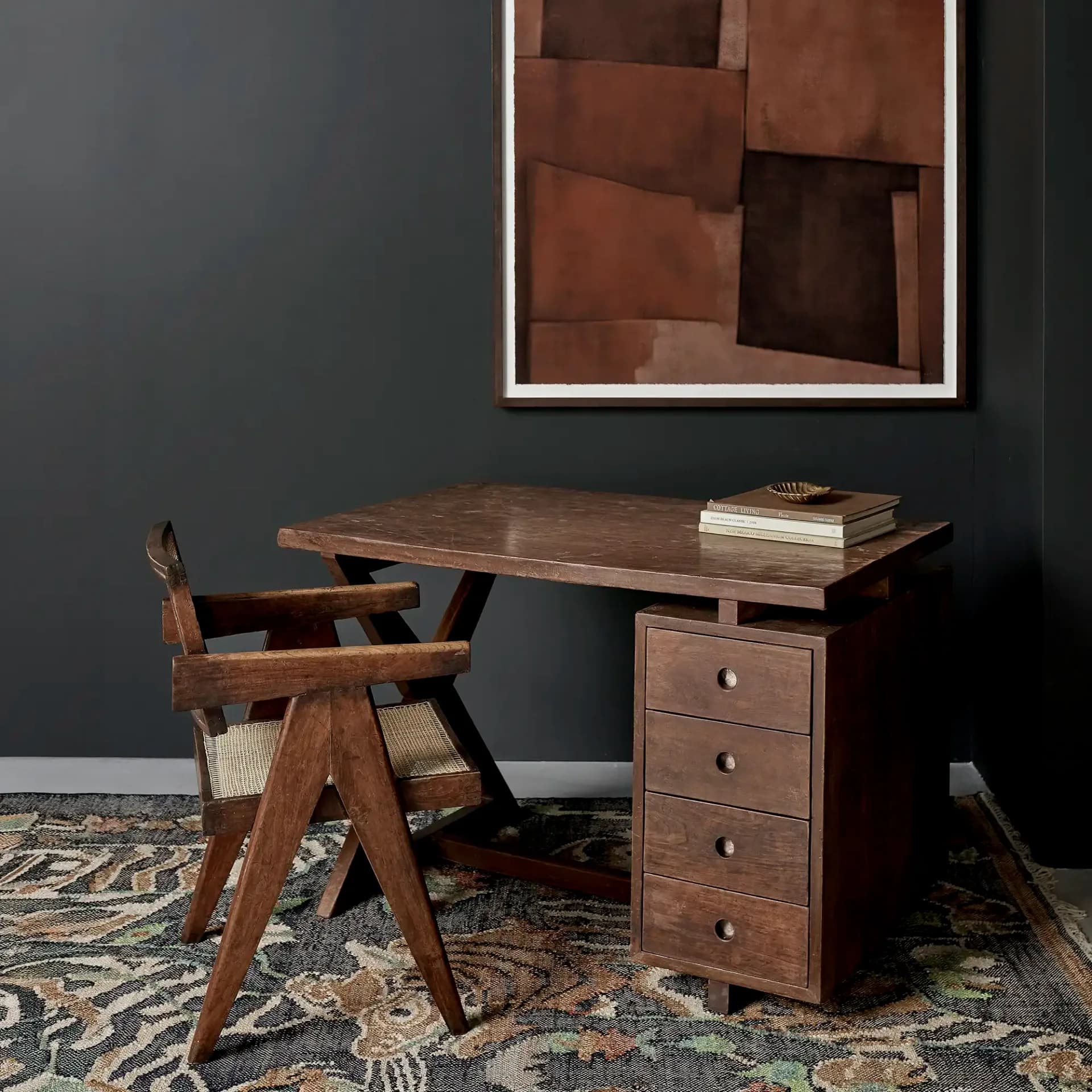 Mid-century modern workspace featuring a walnut desk with four drawers, paired with a sculptural wooden chair with woven seat, against a charcoal wall, styled by Lemieux et Cie.