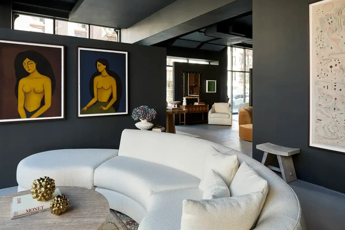 Contemporary living room with curved white sofa, dark charcoal walls, yellow figurative paintings, and polished concrete floors, designed by Lemieux et Cie.