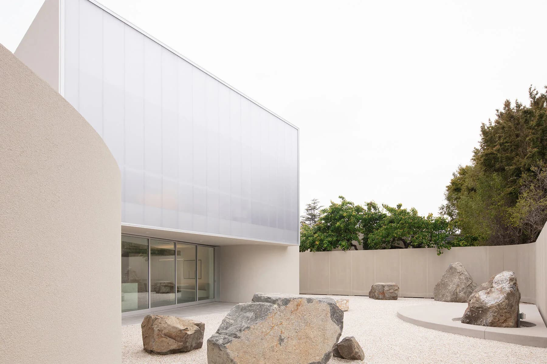 Minimalist courtyard with white cubic volume, polished concrete floor, and scattered boulders, rendered in soft natural light by Leong Leong.