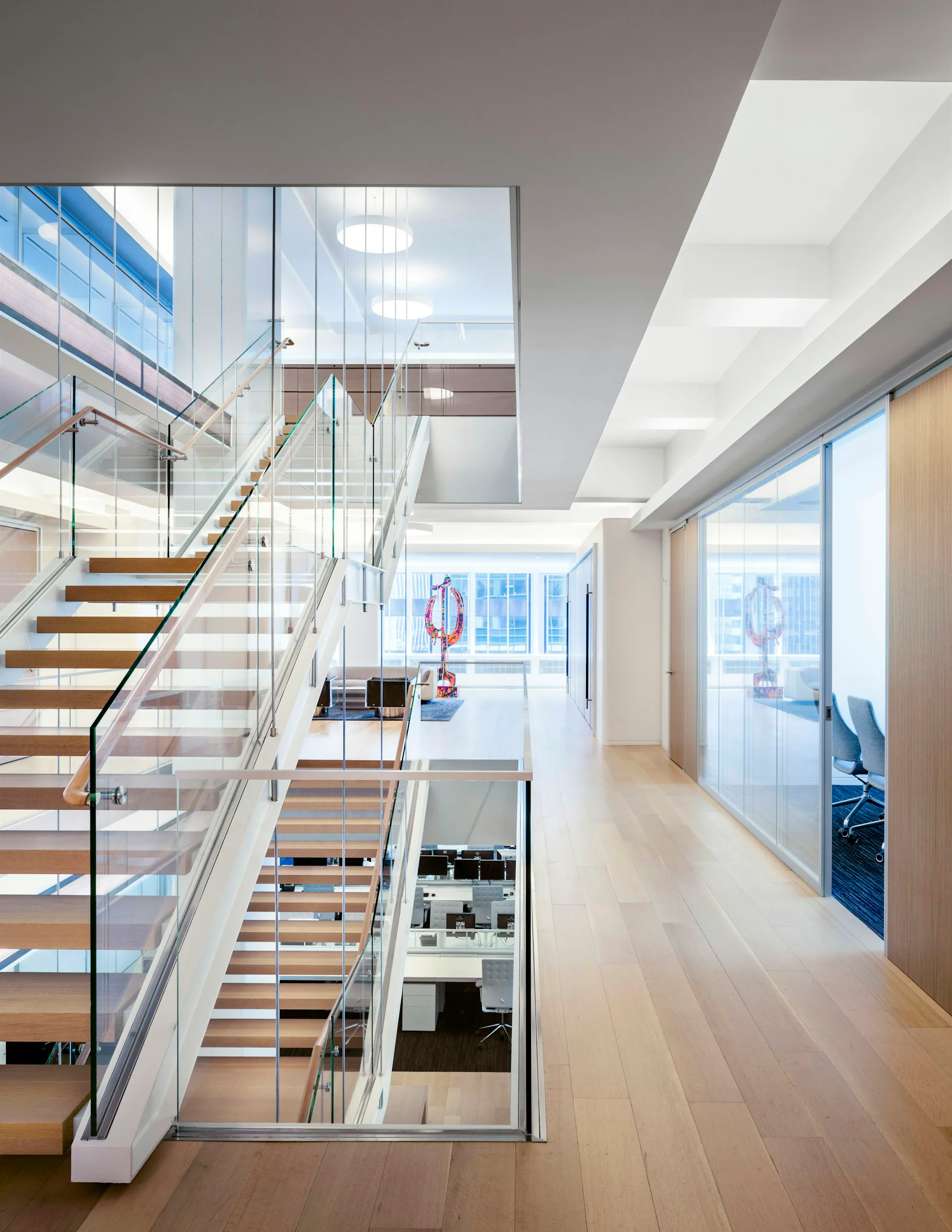Bright multi-level office interior with wooden stairs, glass railings, and floor-to-ceiling windows overlooking city skyline by Leroy Street Studio.