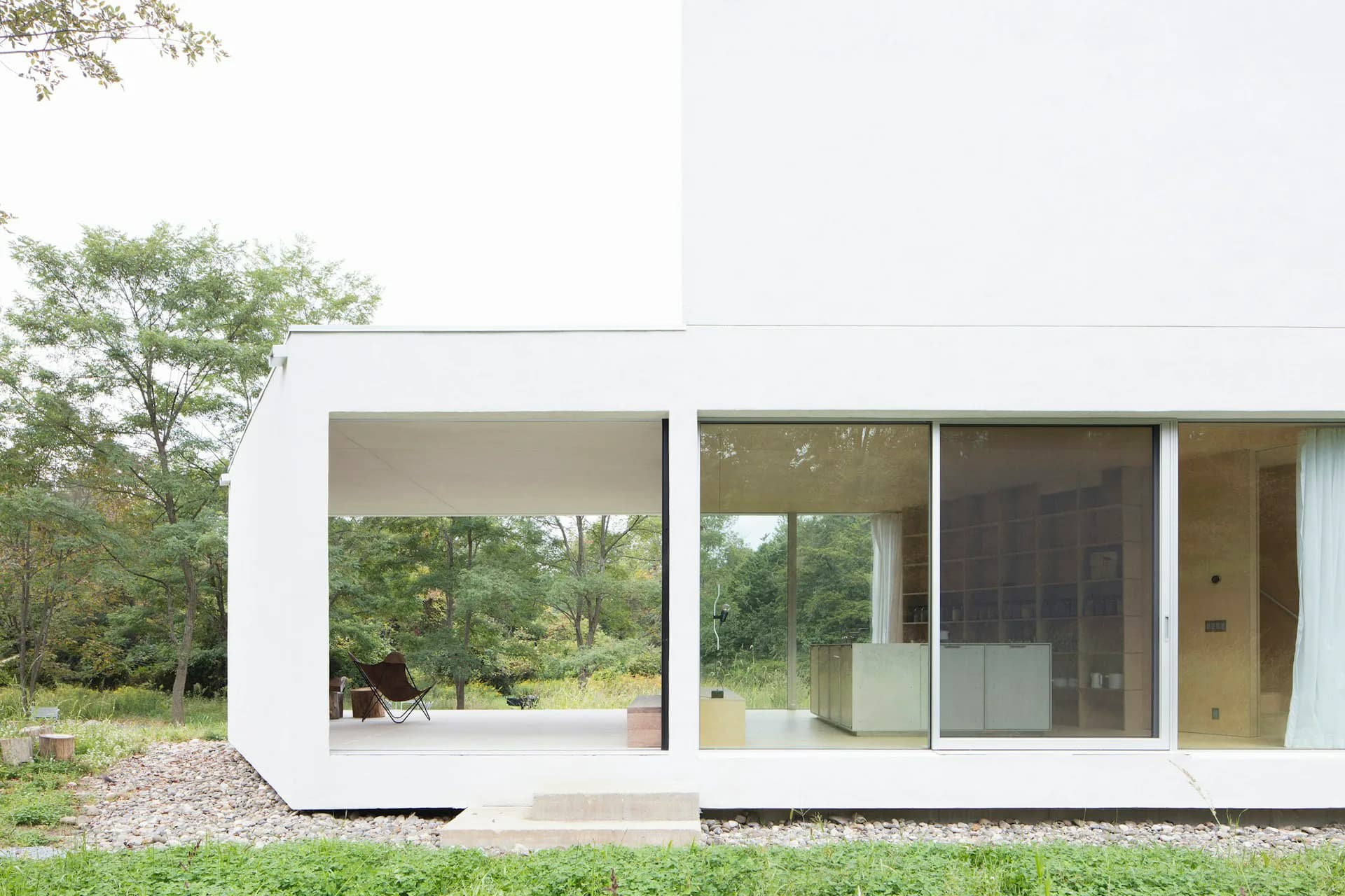 Modern white residential building with curved corner, expansive glazing, and integrated landscape featuring natural surroundings by LEVENBETTS.