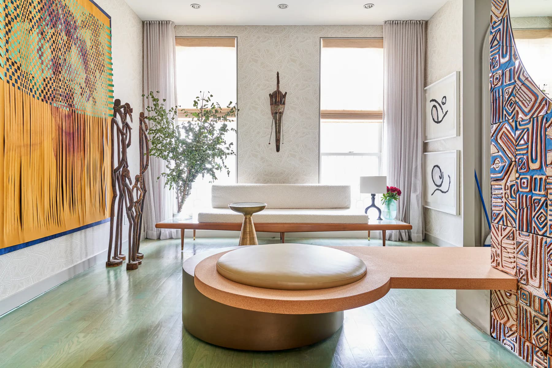 Modern bathroom with round sunken soaking tub, warm wood and brass finishes, patterned textile wall hangings, and large windows with neutral curtains by Leyden Lewis Design Studio.