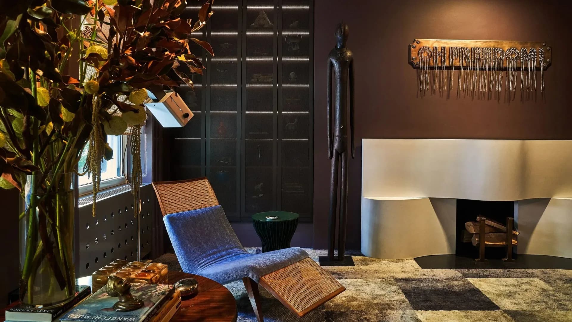 Luxury interior showroom featuring a blue sculptural chair, brass flower arrangement, geometric floor, and modern fireplace with gold accents by Leyden Lewis Design Studio.