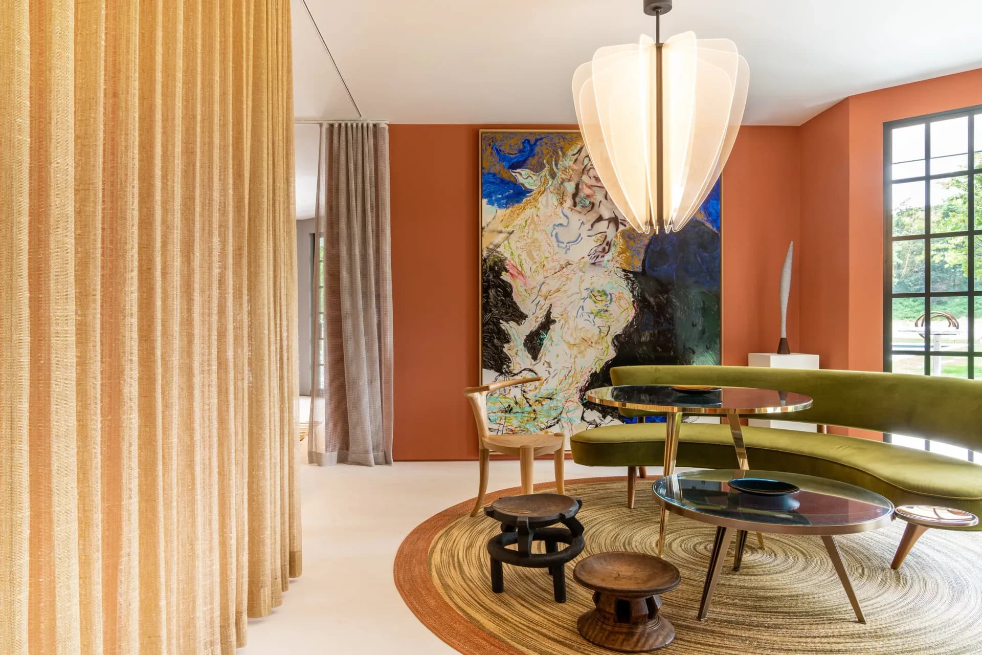 Modern living room with burnt orange walls, green curved sofa, wooden slat partition, abstract artwork, and round patterned rug by Leyden Lewis Design Studio.