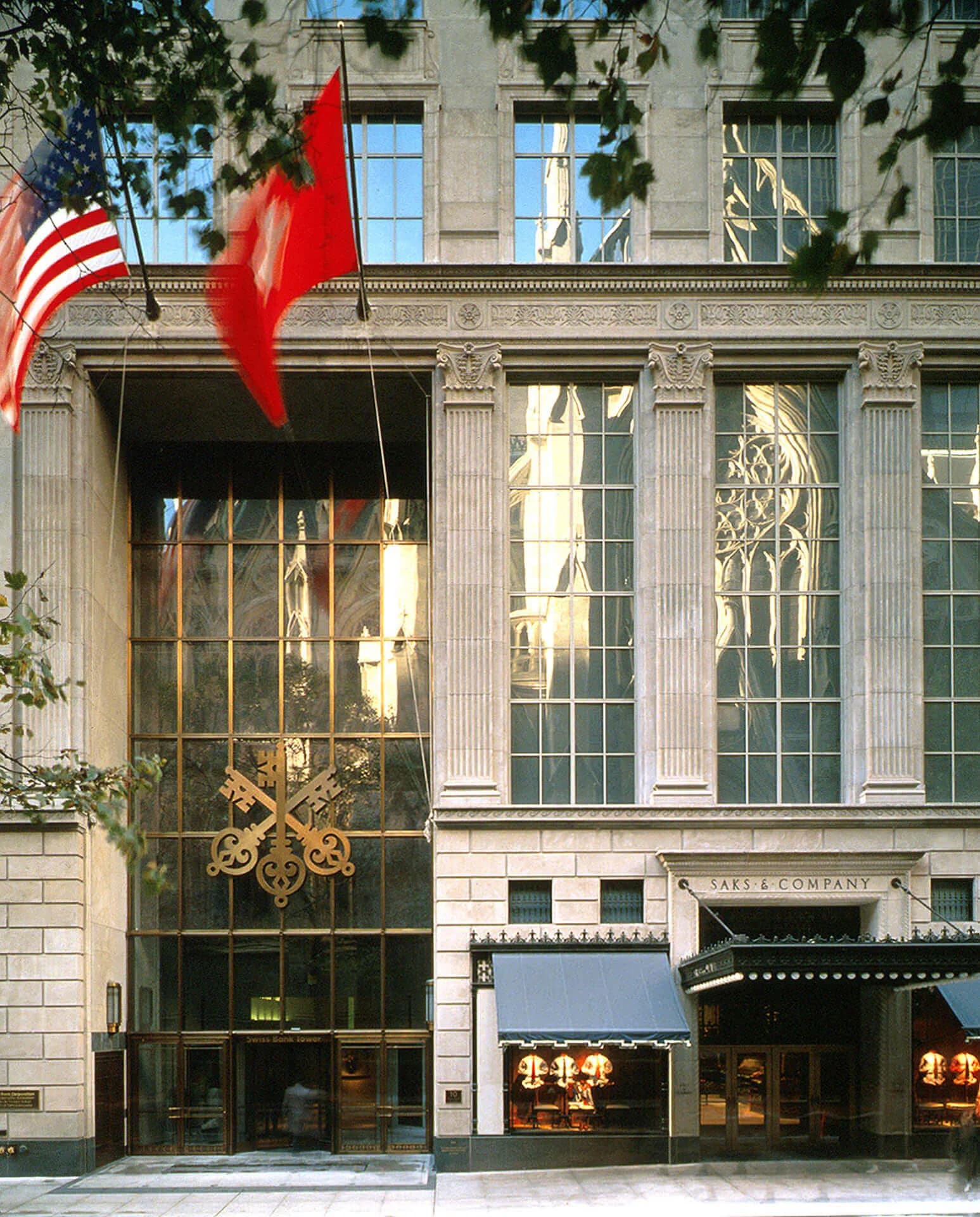 Neoclassical facade with fluted columns, large storefront windows with geometric grillwork, American and red flags, stone ashlar exterior, and ornamental detailing by LHP Architects, PLLC.