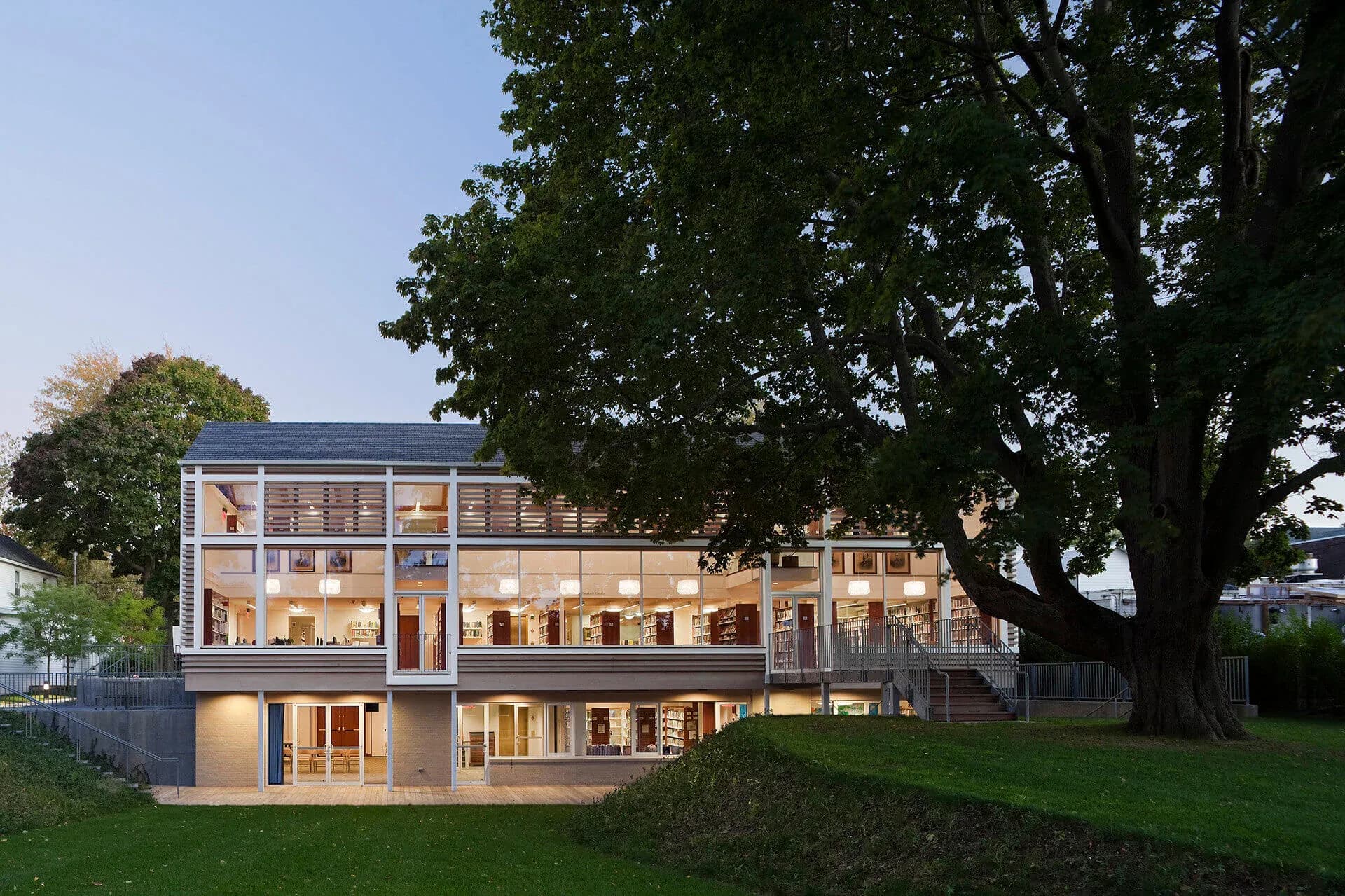 Modern multi-story residential building with glass facades and wooden elements nestled beneath mature trees, designed by LHP Architects, PLLC.
