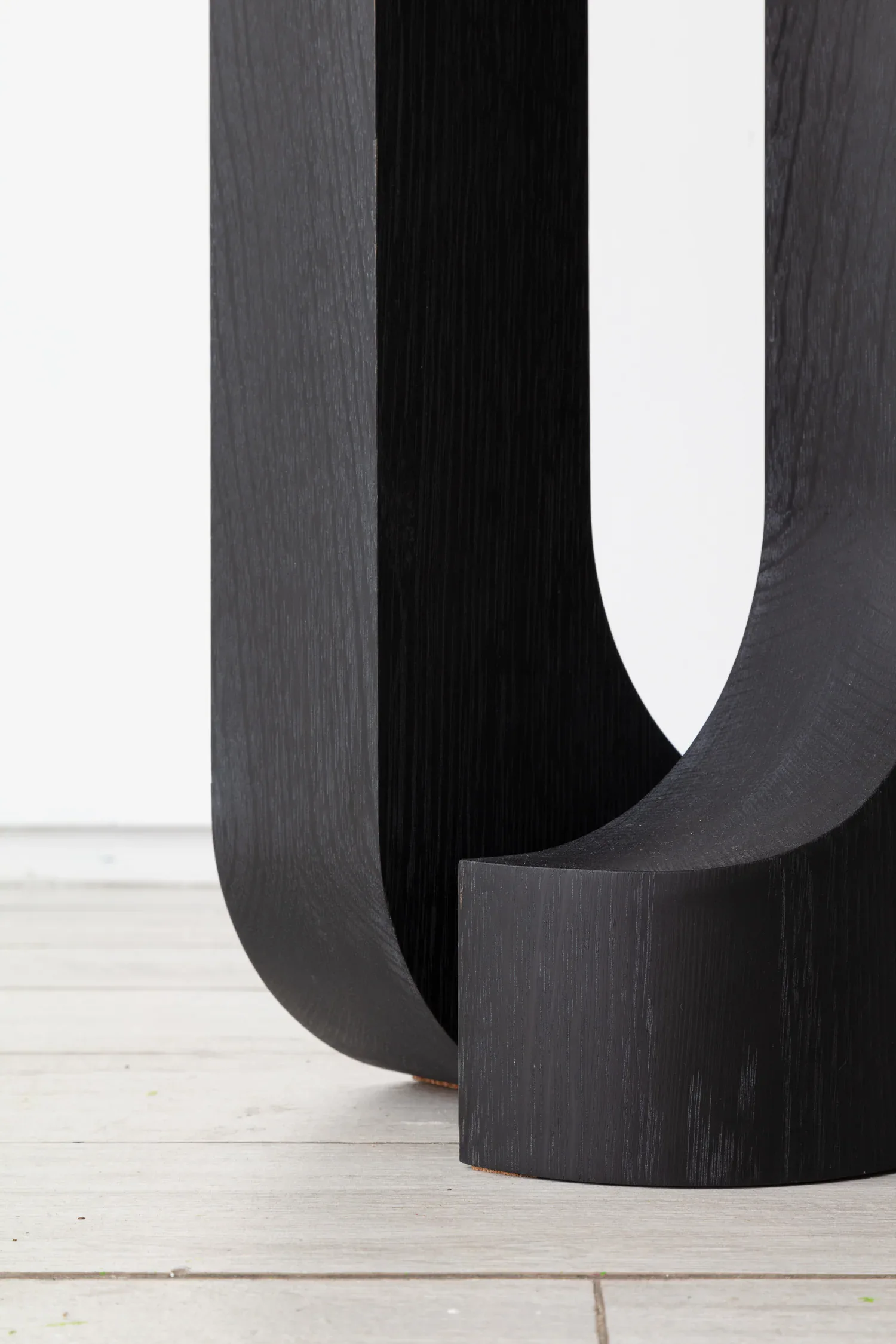 Dark wood curved sculptural installation with organic U-shaped forms and smooth surfaces on a light wooden floor, by Light + Ladder.
