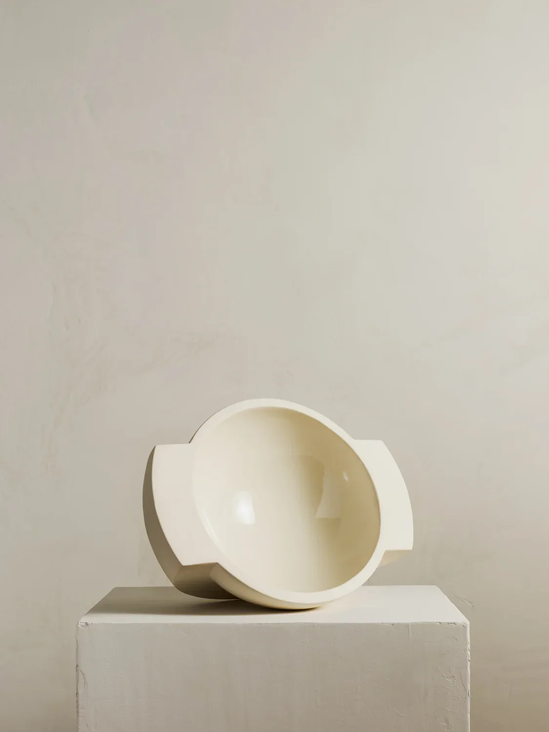 Minimalist ceramic sculptural vessel with organic handles resting on a white plinth against a neutral background by Light + Ladder.