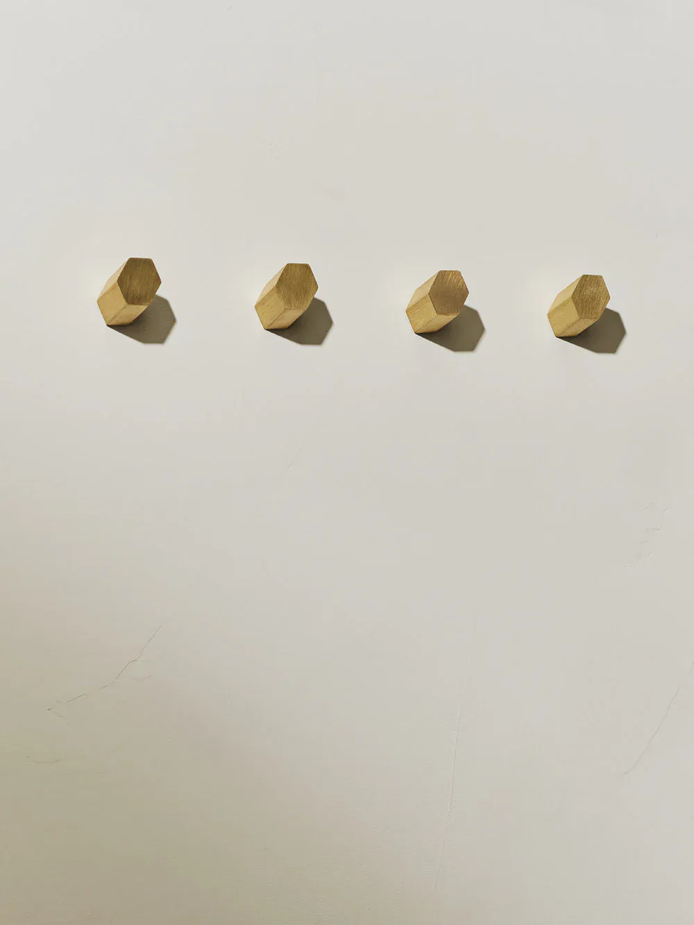 Four brass hexagonal nuts arranged in a row on a neutral background, casting geometric shadows by Light + Ladder.