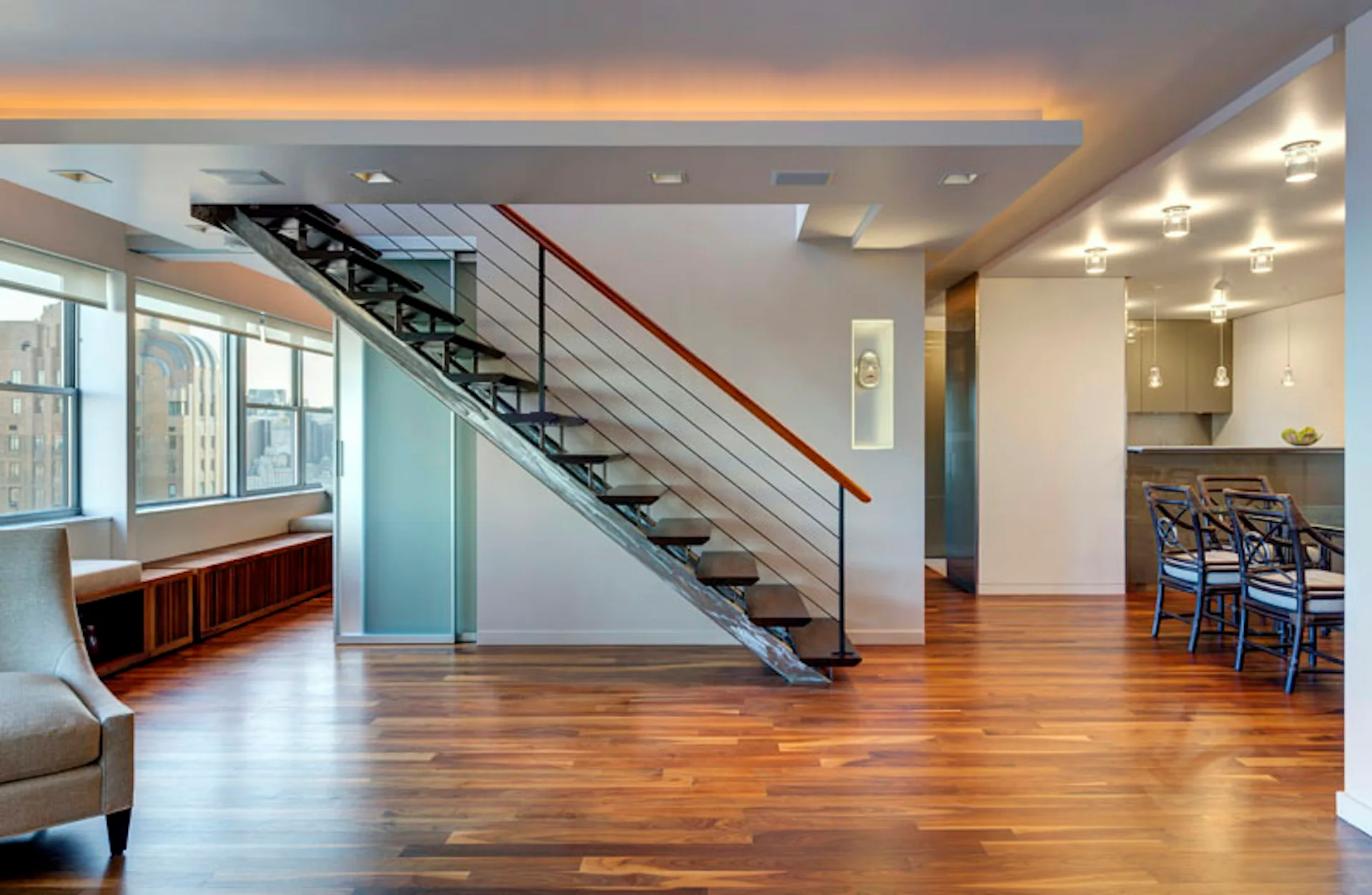 Open-concept loft with warm wood flooring, modern steel and glass staircase with red handrail, and dining area, designed by Lilian H. Weinreich Architects.