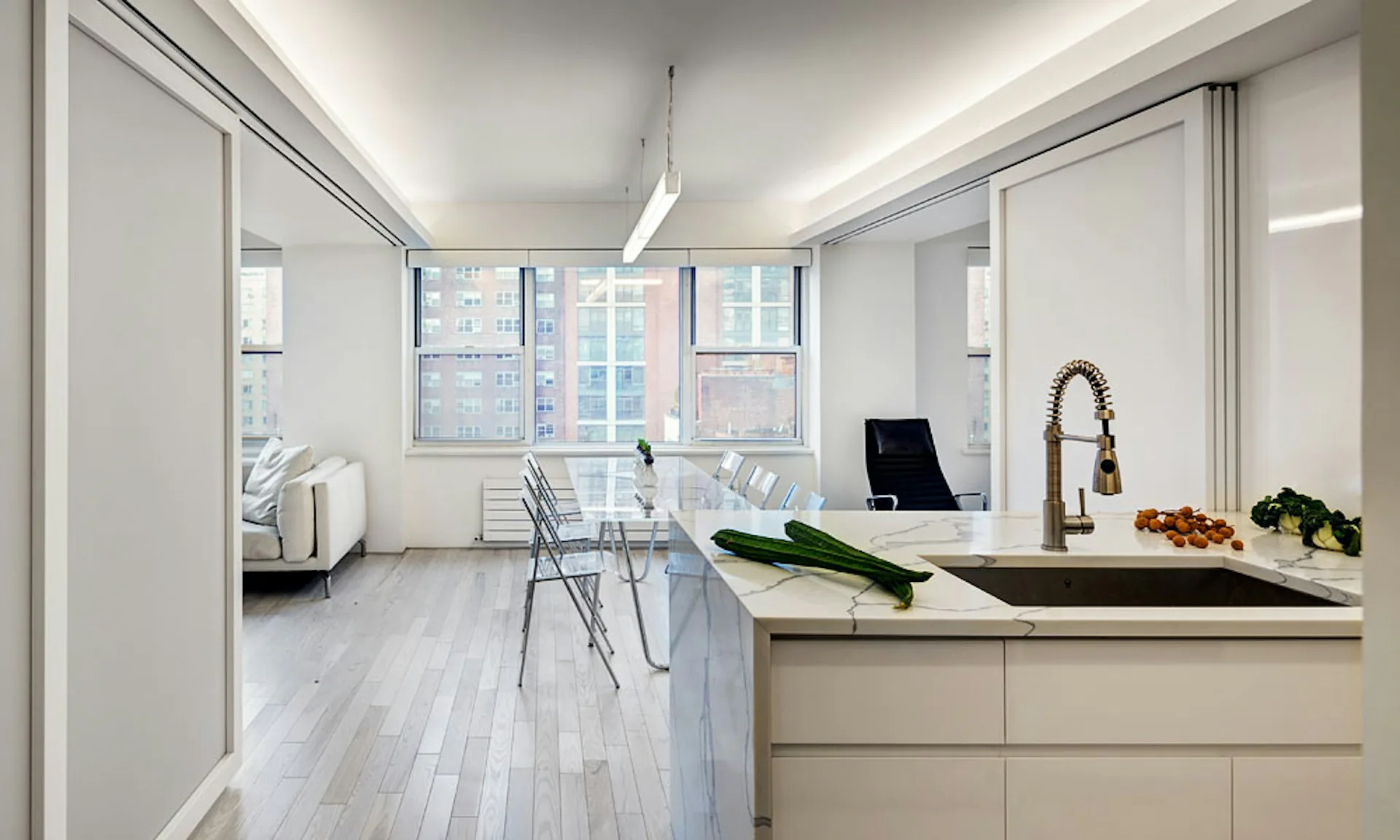 Modern open-plan kitchen and office space with white cabinetry, light wood floors, and floor-to-ceiling windows, designed by Lilian H. Weinreich Architects.