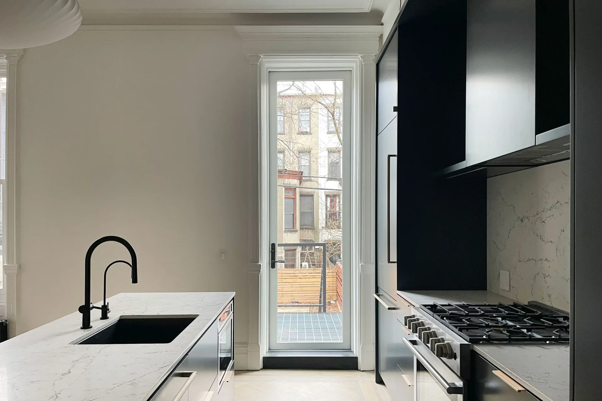 Modern kitchen with white marble countertops, black gas range, matte black faucet, and floor-to-ceiling window by Linearscape.
