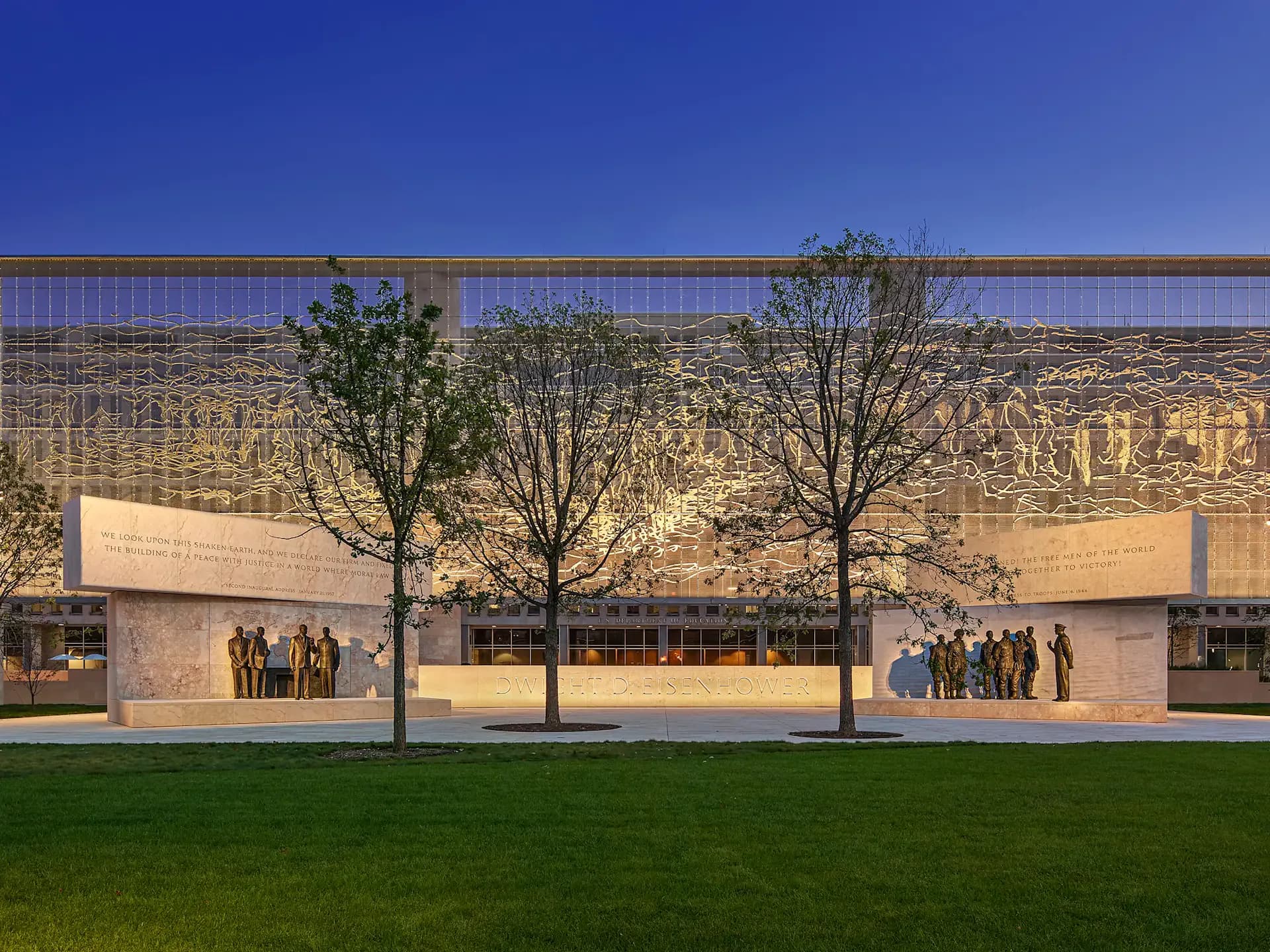 Modern institutional building with cream-colored facades, large glazed upper section, landscaped forecourt with young trees and green lawn, designed by L'Observatoire International.