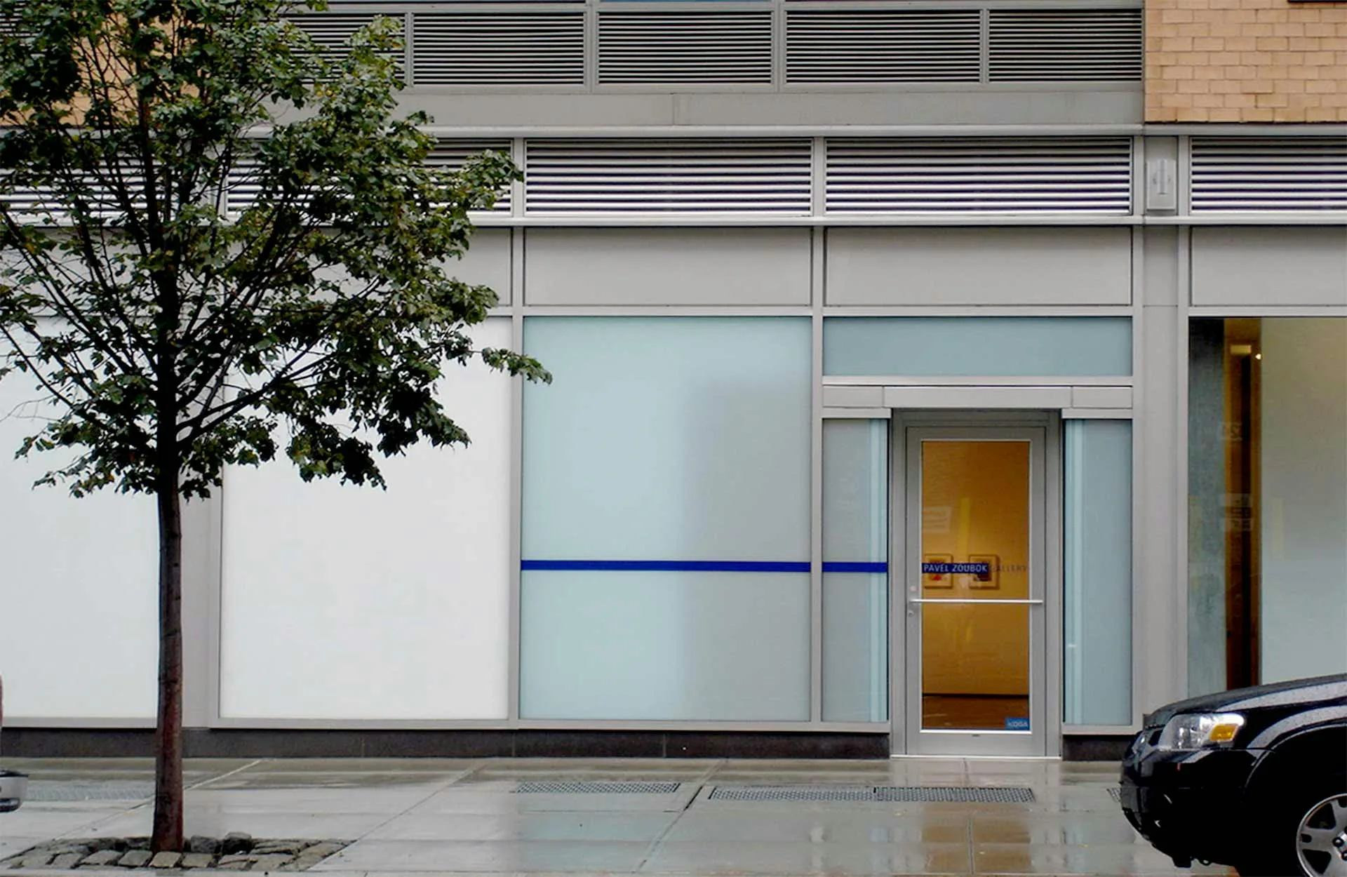Modern storefront with white and light blue glass facade, blue horizontal stripe accent, wooden door, and minimalist design by Louise Braverman Architect.