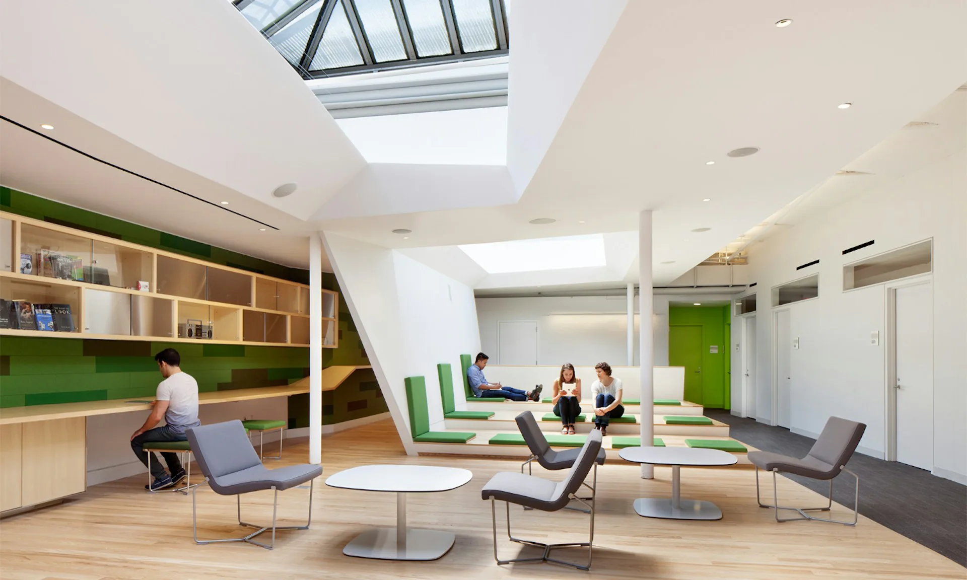 Bright modern office lounge with green accents, skylights, wooden shelving, and collaborative seating areas by LTL Architects.