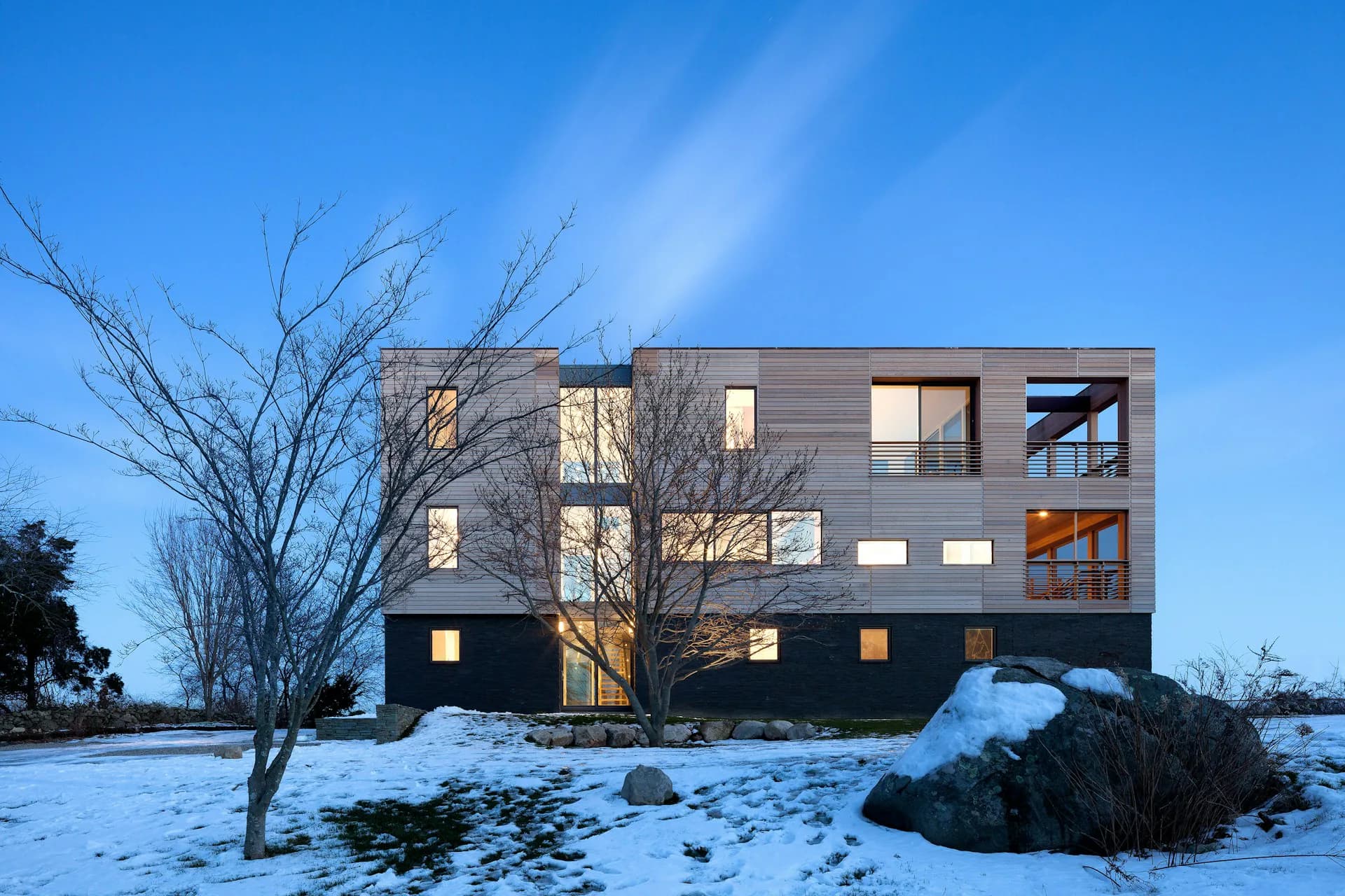 Modern residential building with dark exterior and illuminated windows set in snowy landscape by LUBRANO CIAVARRA ARCHITECTS.
