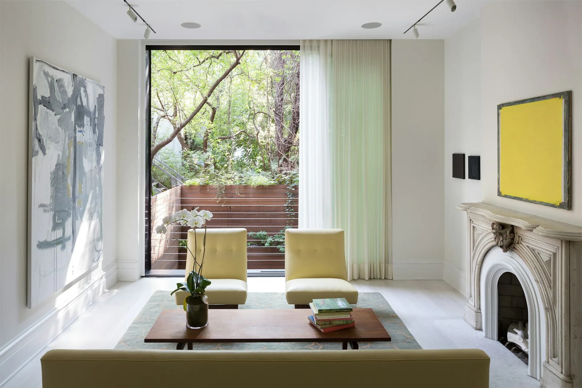 Minimalist living room with white walls, yellow-green upholstered furniture, fireplace, and large glass doors opening to a garden by LUBRANO CIAVARRA ARCHITECTS.