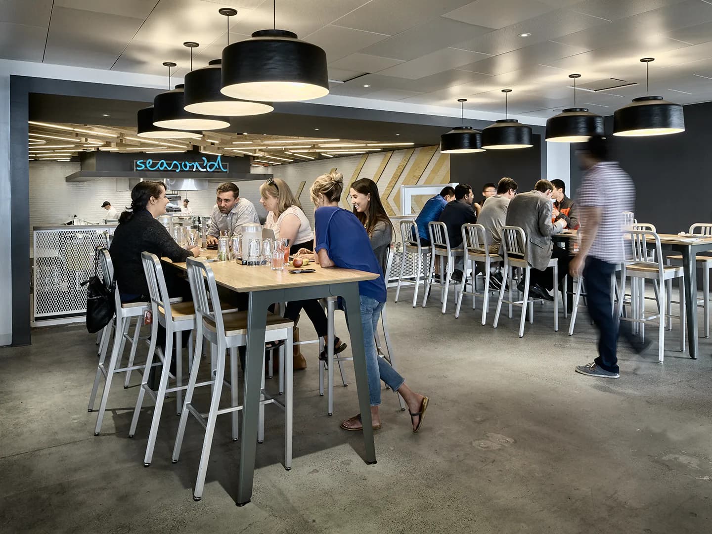Modern cafeteria with concrete floors, white bar seating, black pendant lighting, and casual gathering spaces designed by Lumen Architecture.