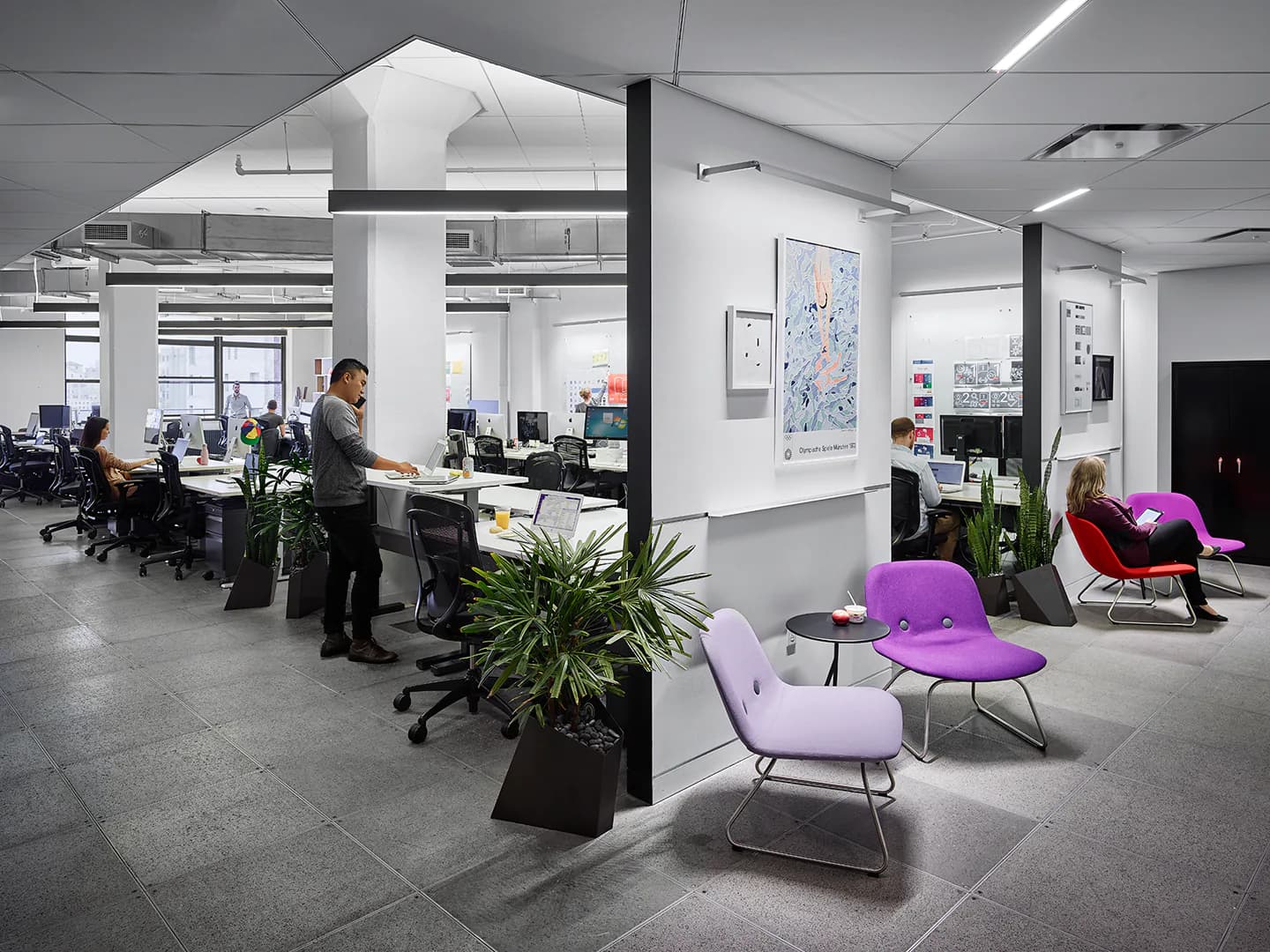 Modern open-plan office with polished concrete floors, white walls, structural columns, colorful seating areas, and abundant natural light by Lumen Architecture.