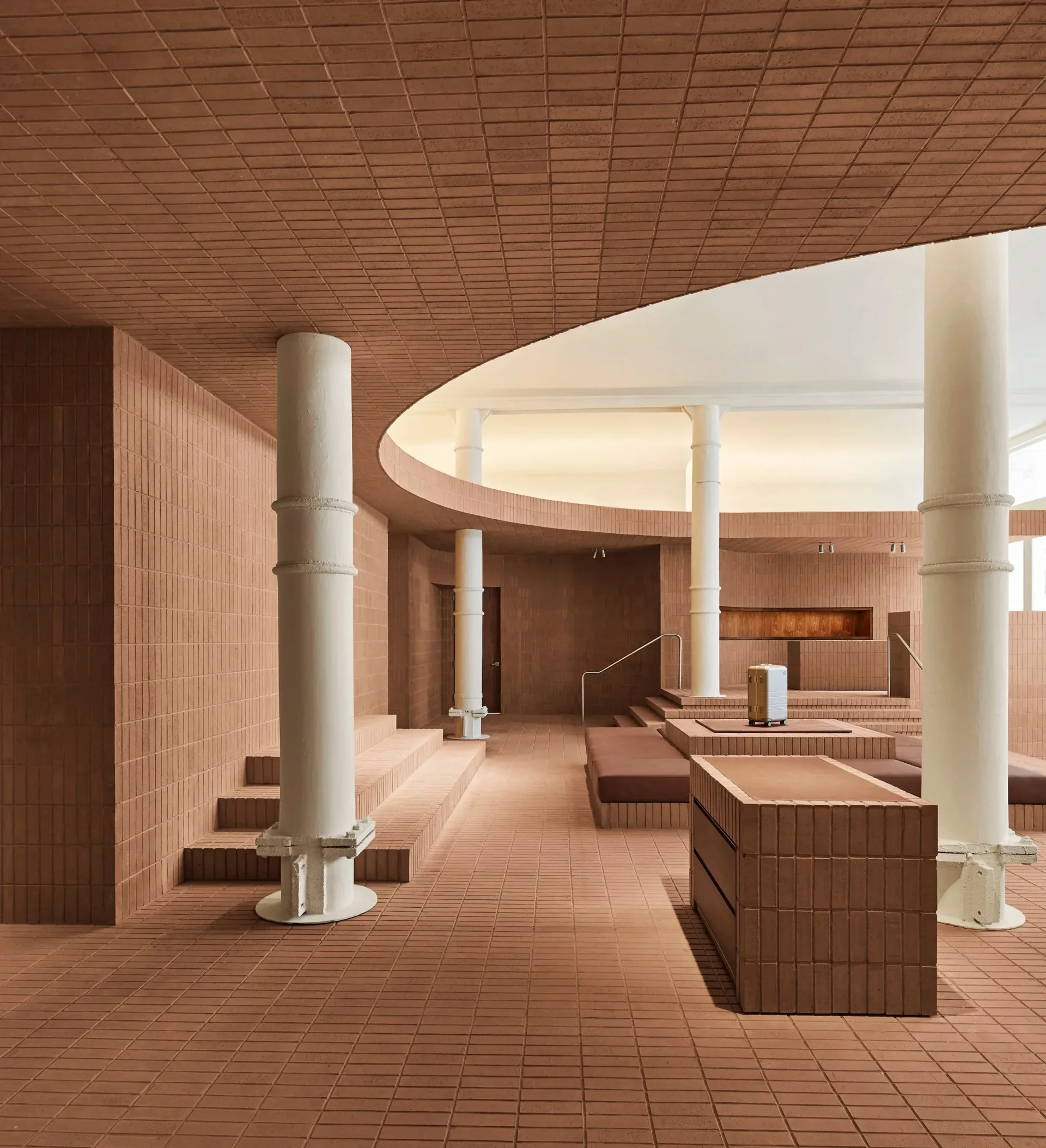 Warm terracotta-toned interior with cylindrical columns, curved ceiling elements, and geometric brick detailing throughout the minimalist space by Lux Collaborative.