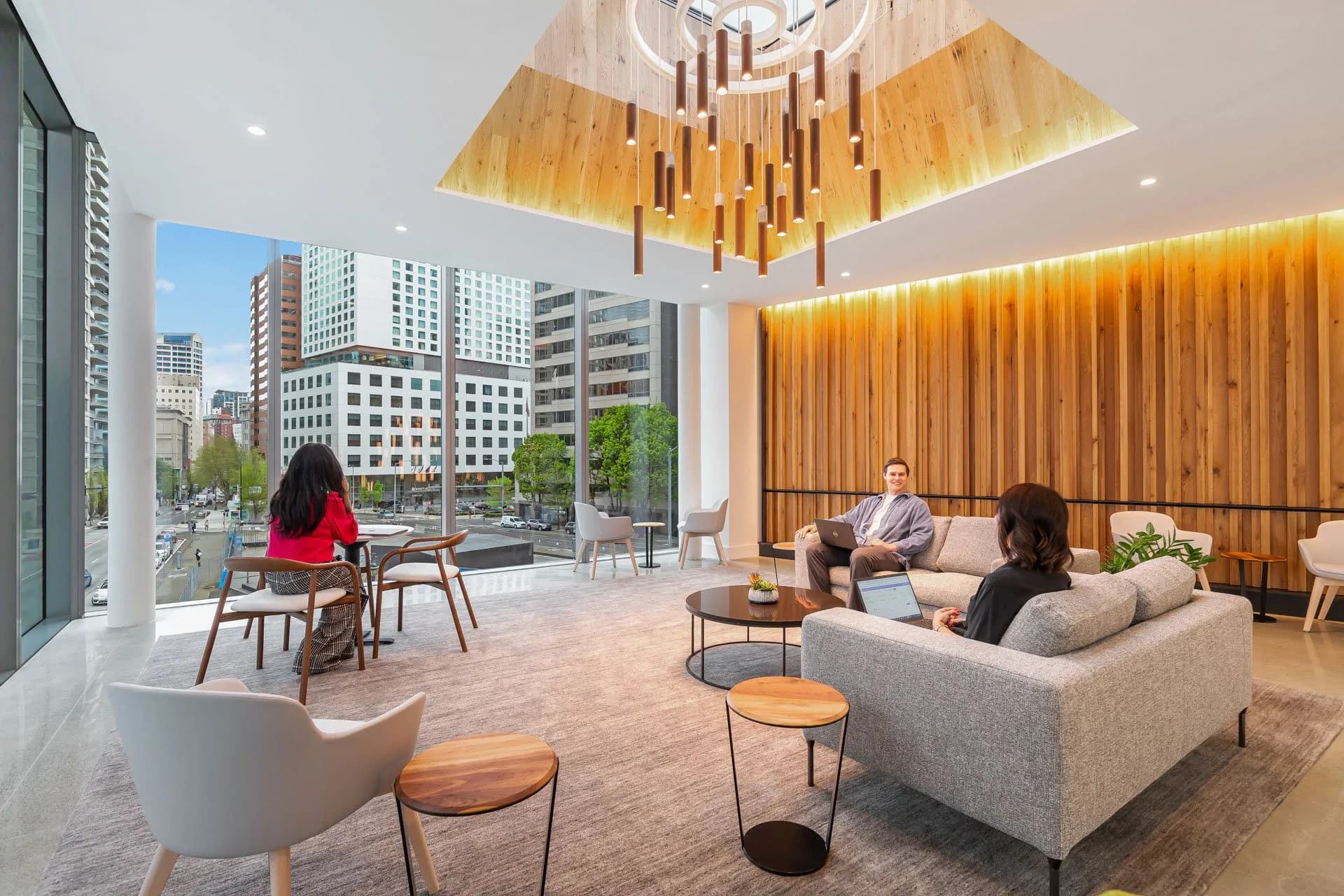 Modern luxury lounge with warm wood ceiling panels, gray upholstered seating, and floor-to-ceiling windows overlooking a city skyline, designed by Lux Collaborative.