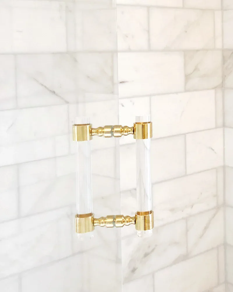 Luxe brass and lucite door pulls mounted on marble subway tile wall with soft natural light casting geometric shadows, by LuxHoldUps.