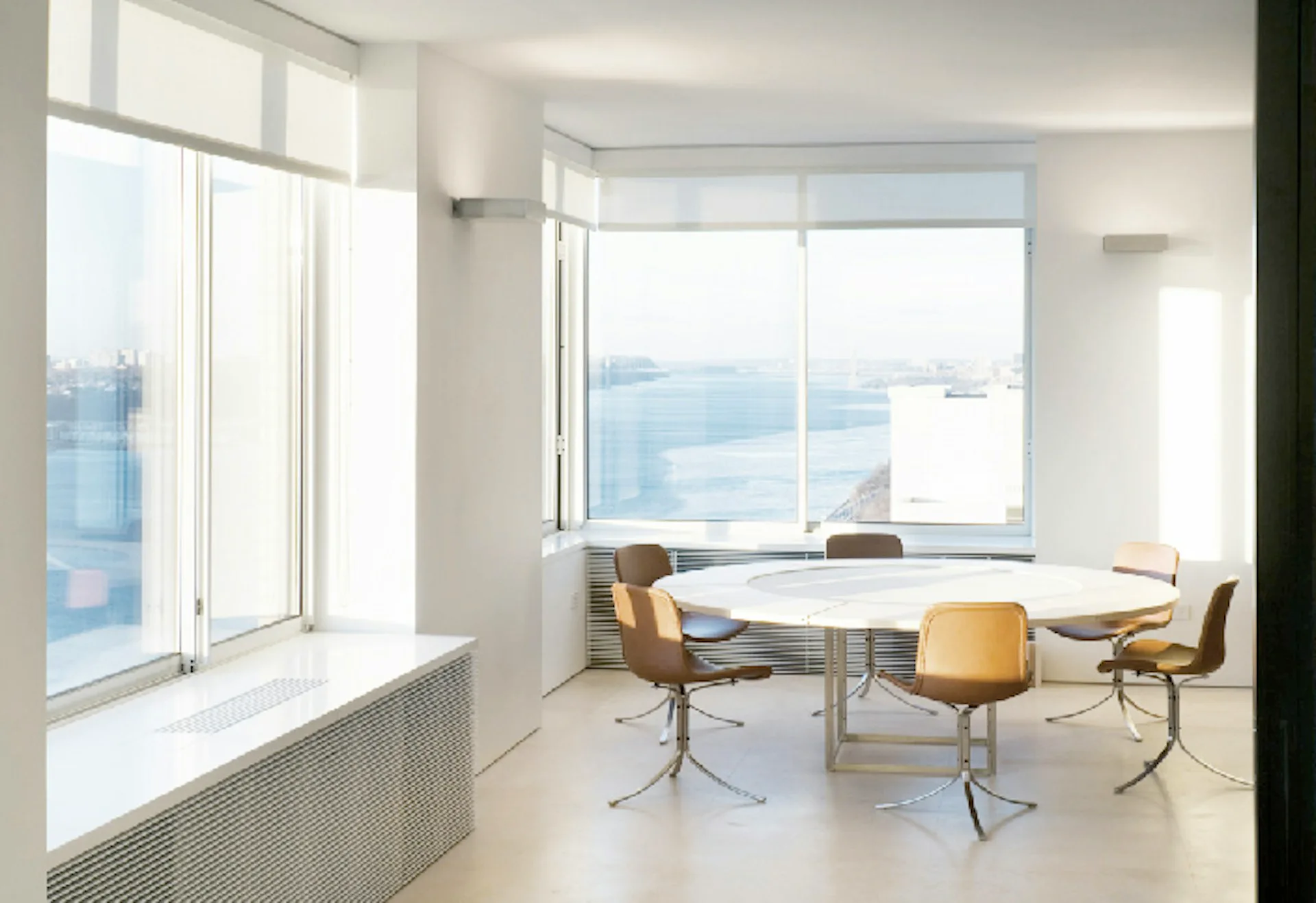 Minimalist office interior with floor-to-ceiling windows overlooking water, featuring a simple desk, four modern chairs, and neutral palette by LYNCH EISINGER DESIGN Architects.
