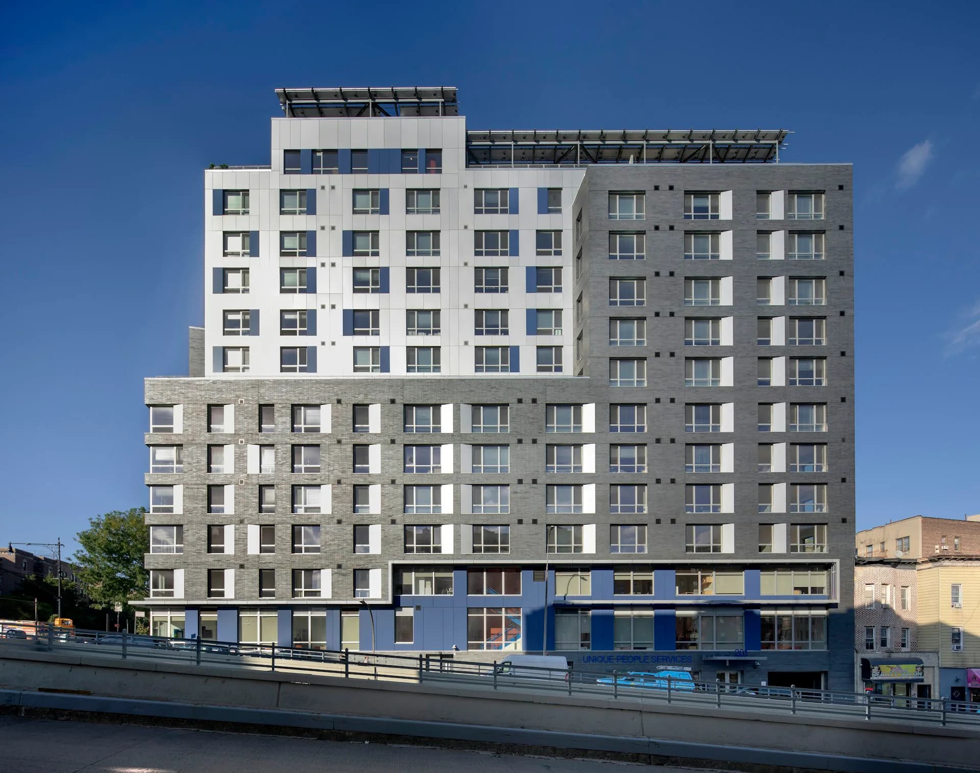 Contemporary residential building featuring stacked white and gray facade modules with regular window patterns, blue commercial ground floor, and integrated waterfront promenade by Magnusson Architecture and Planning, PC.