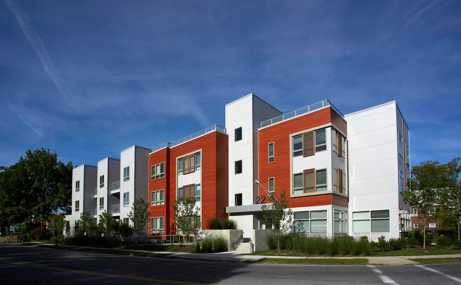 Modern residential building with alternating red-orange and white facades, featuring multiple stories, large windows, and ground-floor commercial space by Magnusson Architecture and Planning, PC.