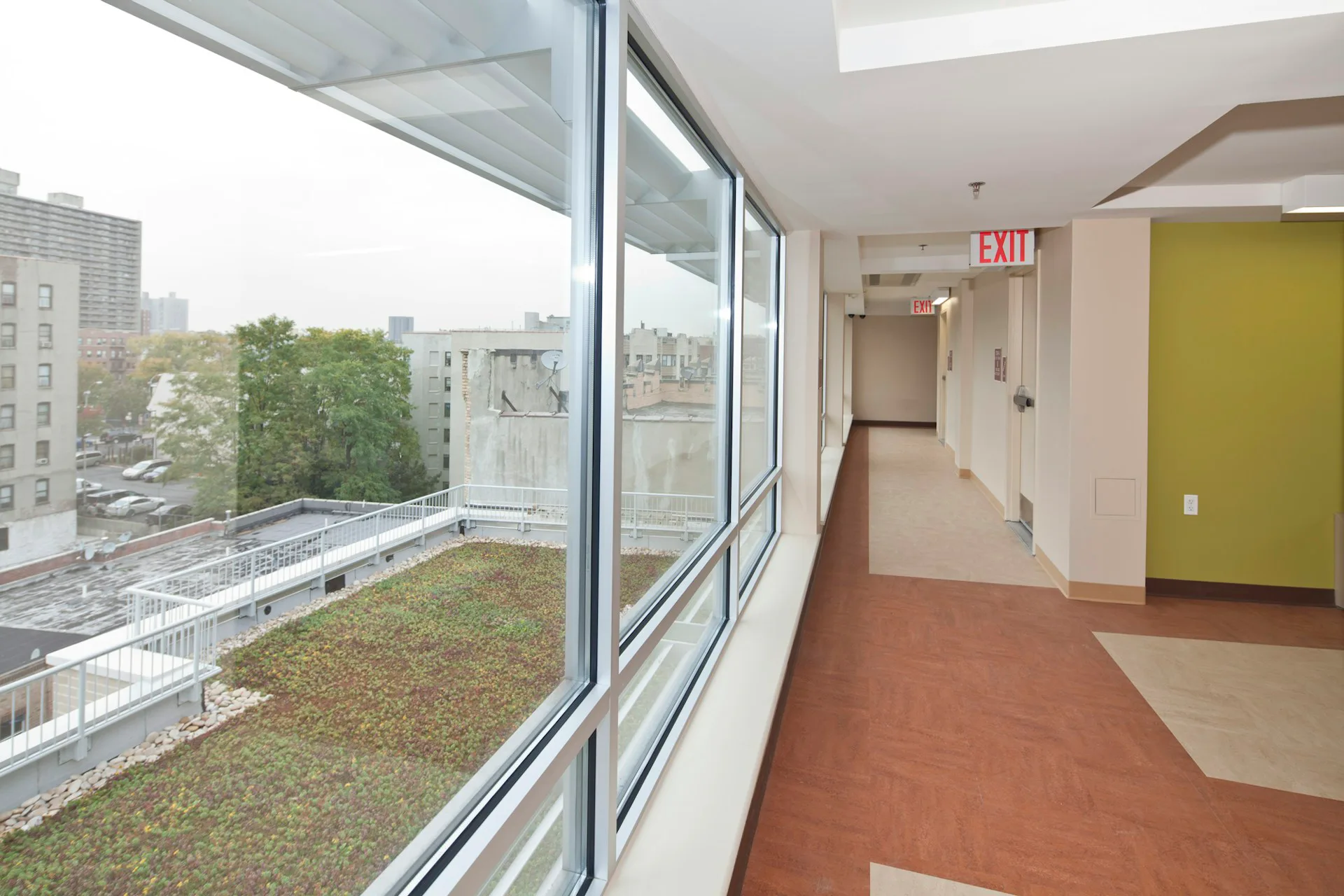 Modern corridor with expansive glazed windows overlooking a green roof terrace, terra cotta flooring, and bright yellow accent wall by Magnusson Architecture and Planning, PC.