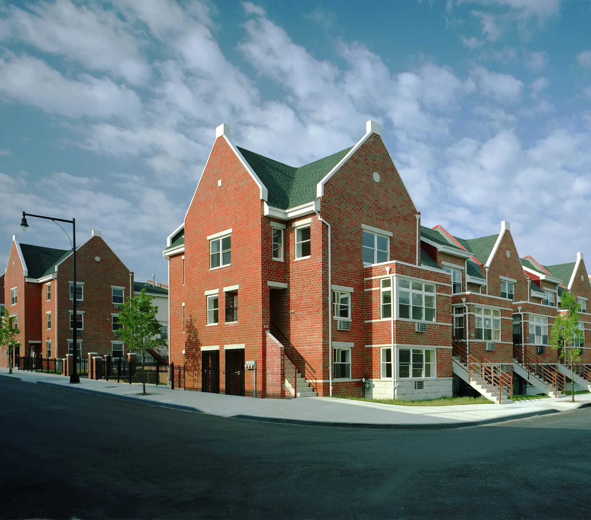 Brick residential townhouse complex with green gabled roofs, multiple units with large windows and stone accents, rendered street view by Magnusson Architecture and Planning, PC.