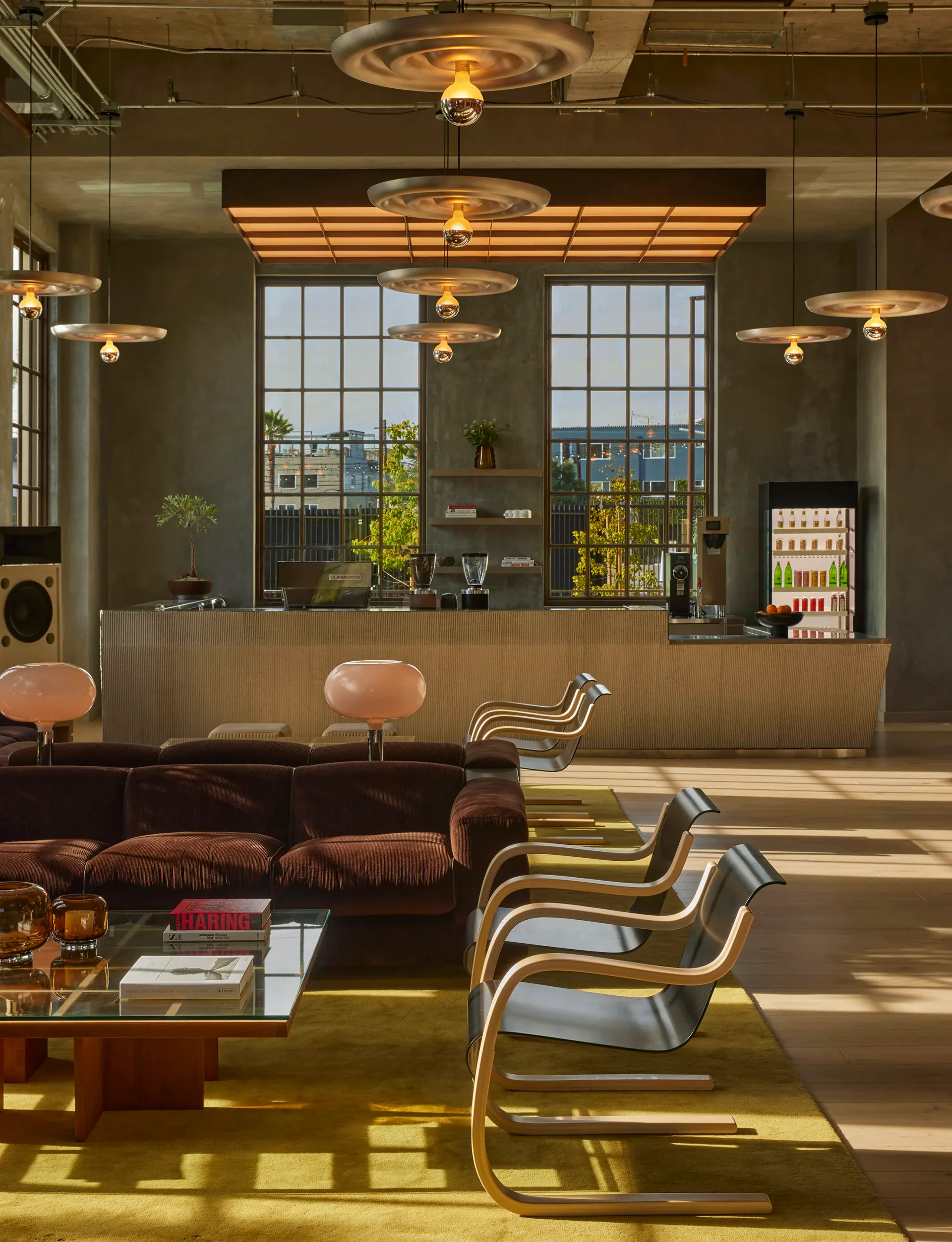 Modern reception area with warm bronze finishes, sculptural pendant lighting, floor-to-ceiling windows overlooking cityscape, and curved seating by Map Design Studio.