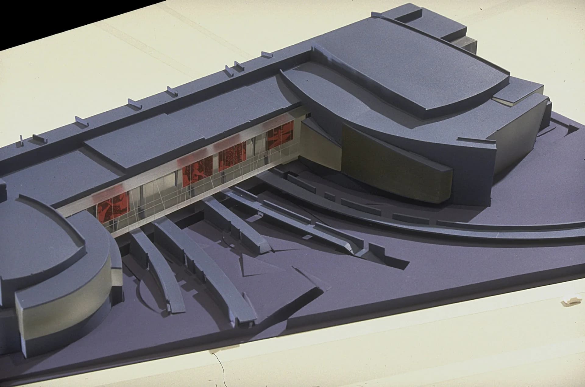 Architectural model or rendering of a modern curved building complex with purple-toned surfaces, featuring a recessed storefront and flowing sculptural forms by Marble Fairbanks.