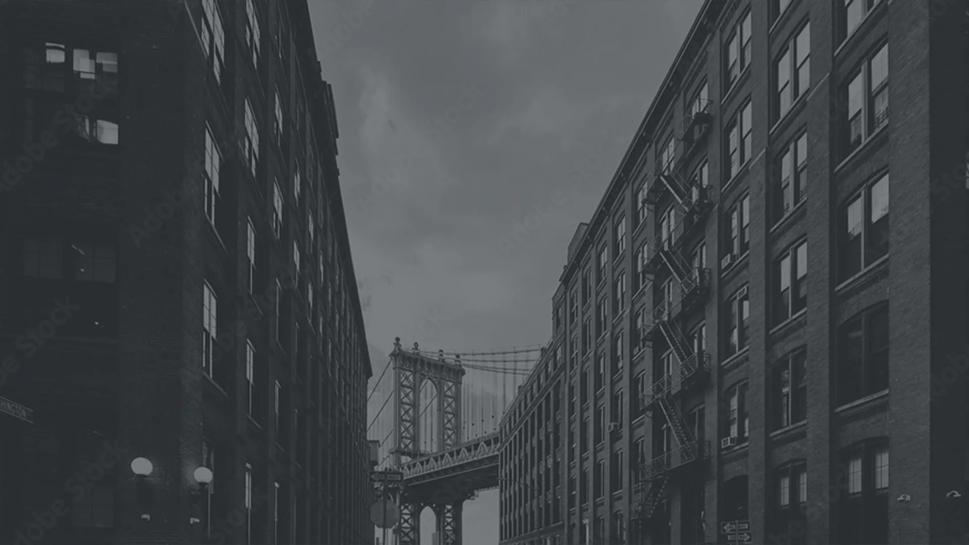 Monochromatic street view of Manhattan Bridge framed between tall brick buildings in dramatic urban architectural composition by Mark Jupiter.