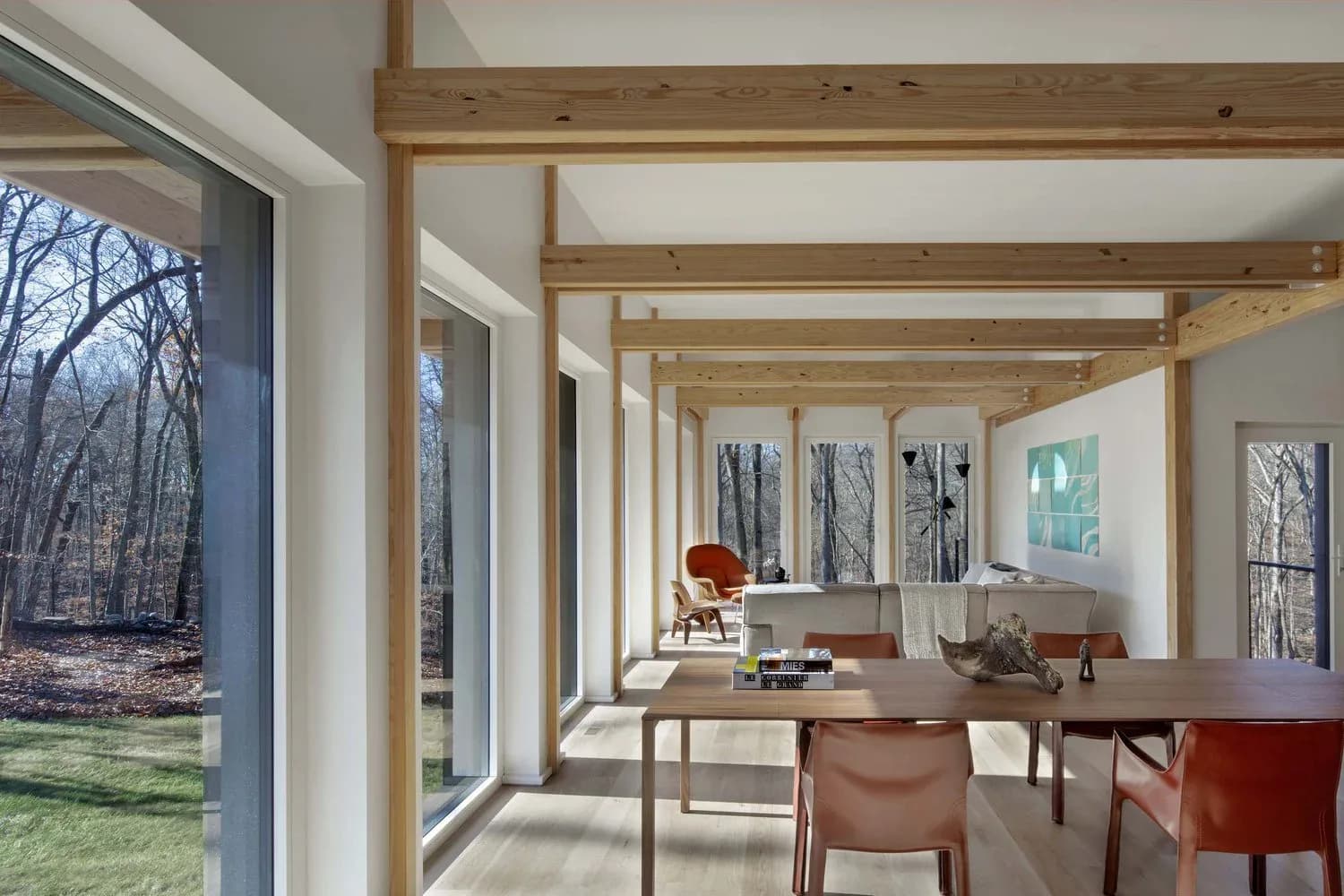 Modern interior workspace with floor-to-ceiling windows, wooden beam ceiling structure, mid-century furniture, and natural light flooding across wood tables and leather chairs by Marner + Marner.
