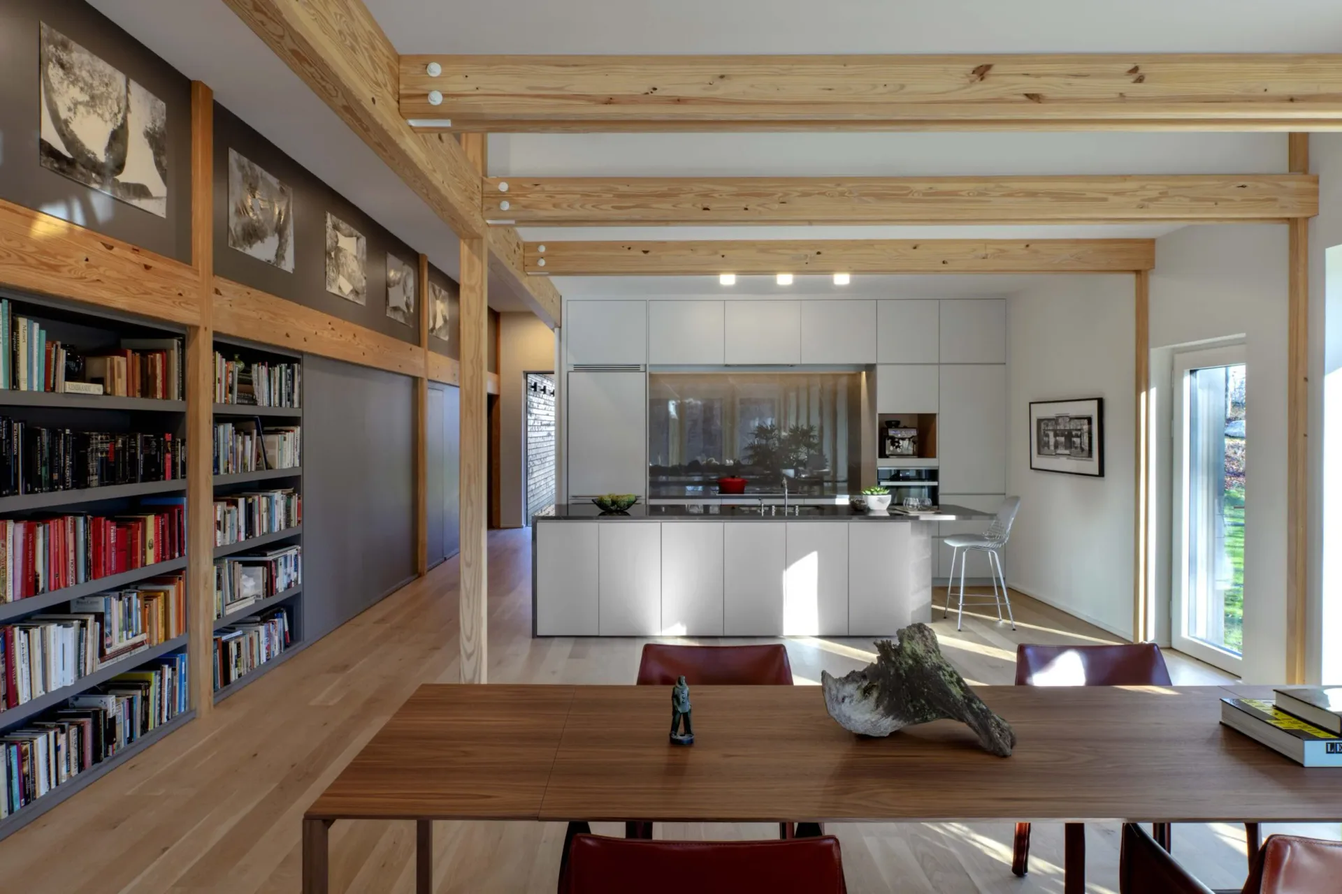 Bright open-plan interior with wooden beams, built-in bookshelves, minimalist kitchen, dining table, and abundant natural light by Marner + Marner.