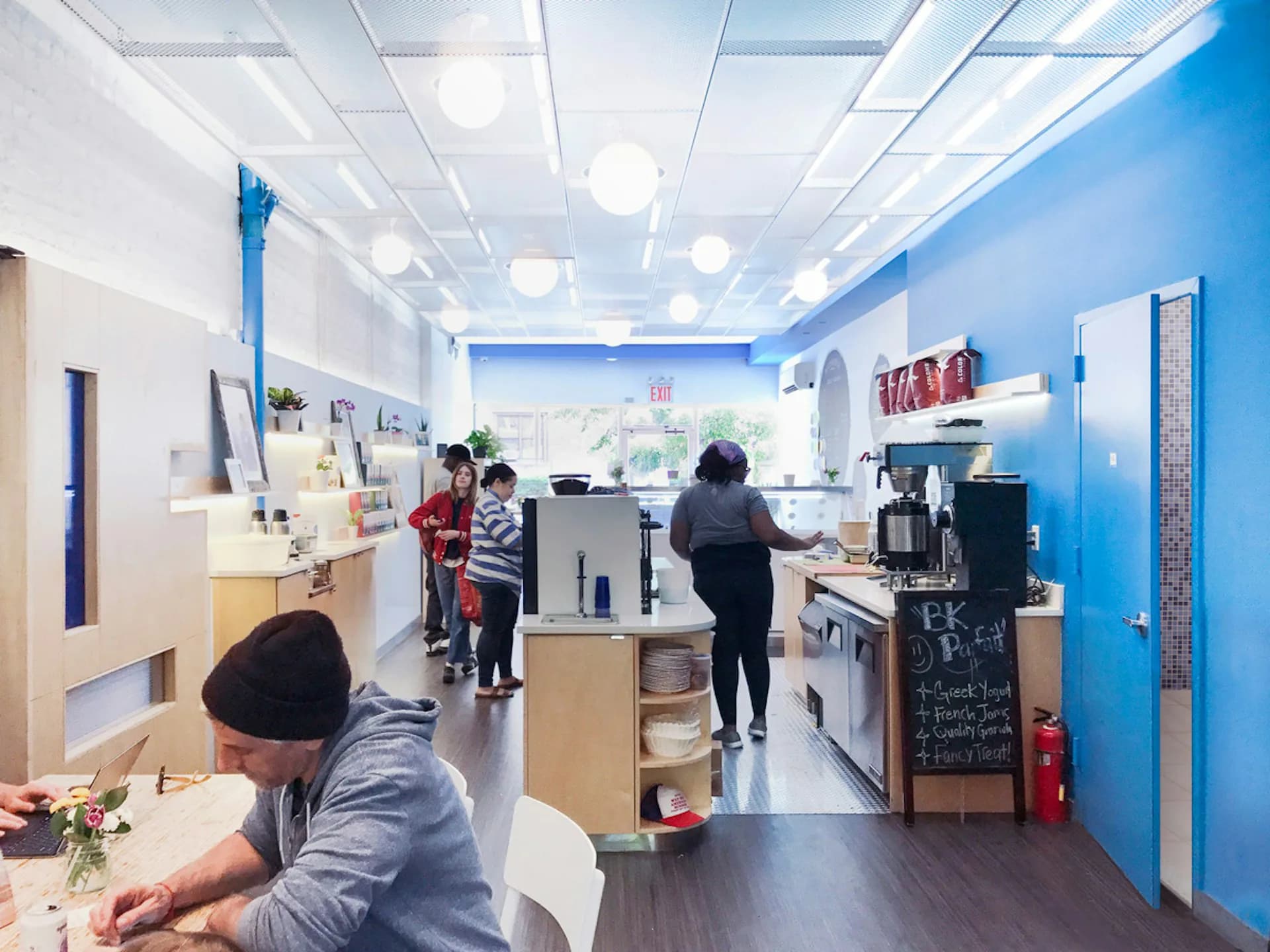 Bright retail interior with blue accent walls, white ceiling with integrated lighting, natural wood shelving, and service counter, designed by Marpillero Pollak Architects.