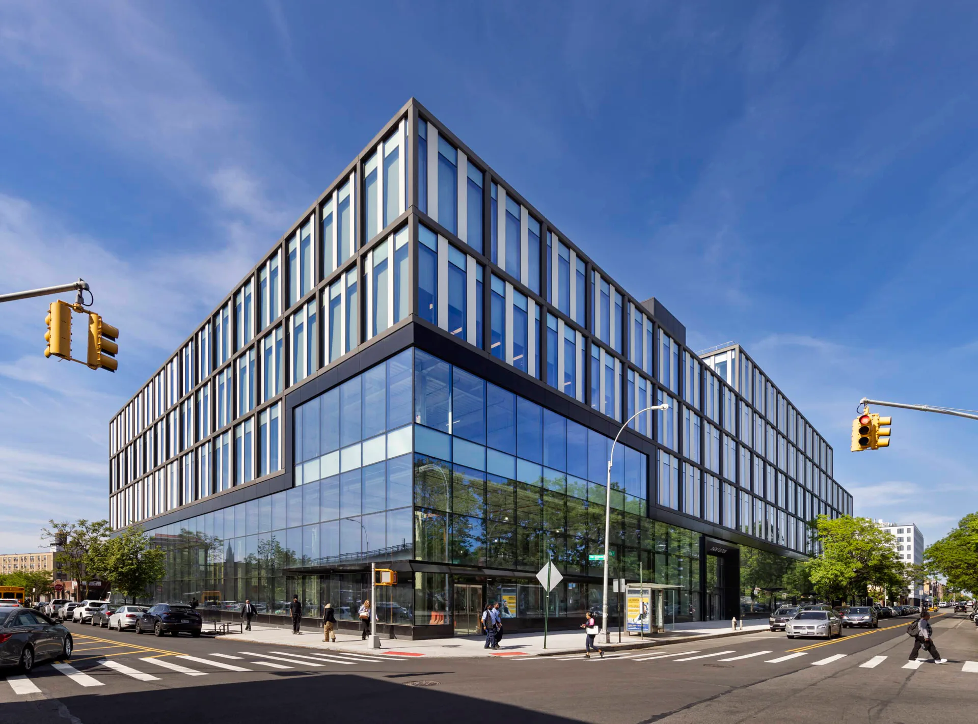 Modern corner building with glass facade and vertical striping, street-level retail spaces, pedestrians and urban context, architectural photography by Marvel.