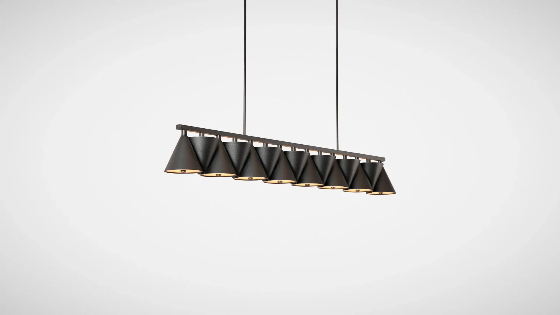 Linear pendant light fixture with geometric triangular shade elements in dark metal, suspended by two cables against a neutral background, by Matter Made.