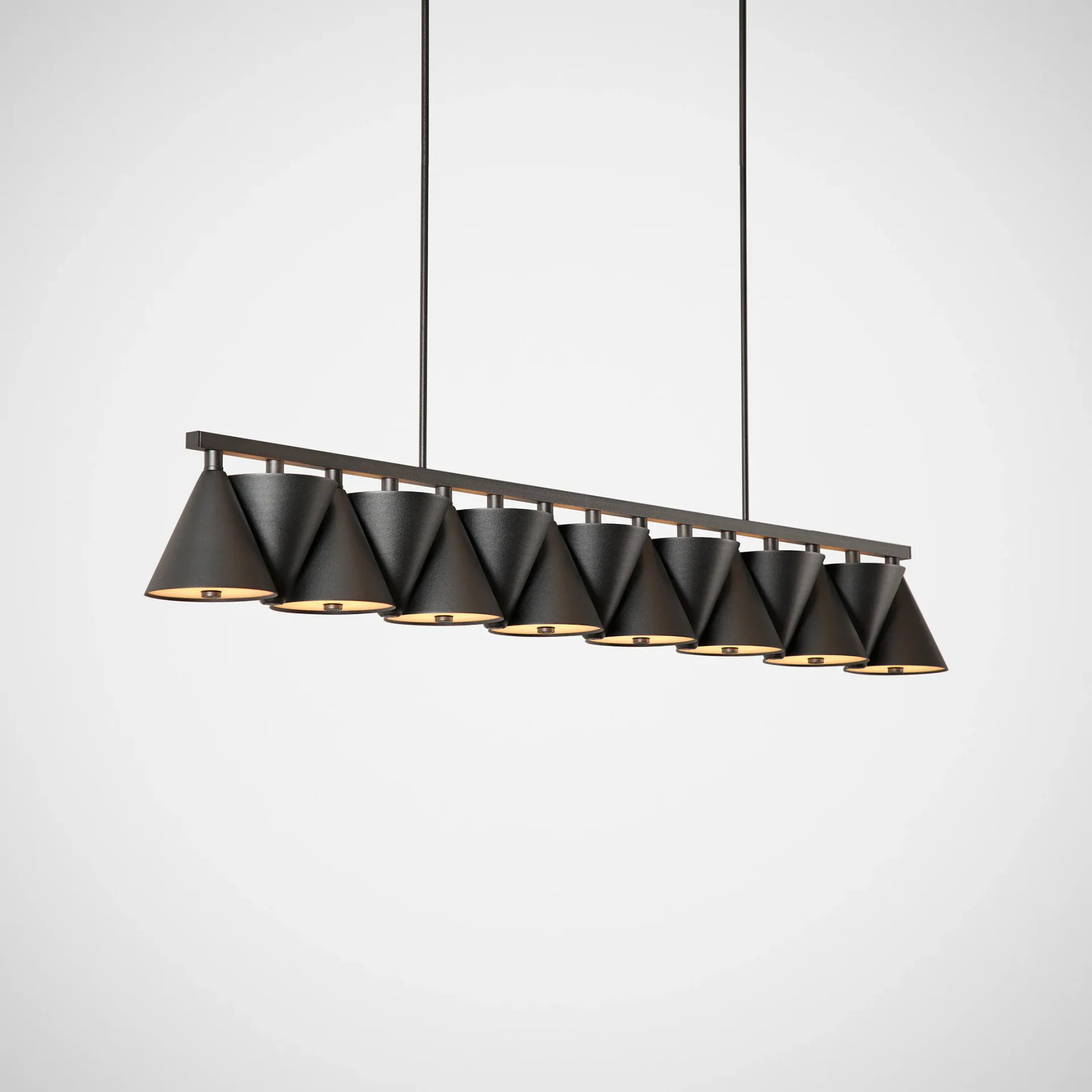 Linear pendant light fixture with multiple black cone-shaped shades and gold interior detailing suspended from ceiling by Matter Made.