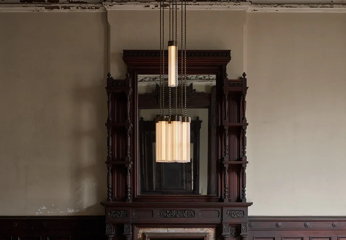 Dark wood-framed architectural niche with hanging cylindrical pendant light fixture suspended by chains, showcasing modern lighting design within classical millwork by Matter Made.