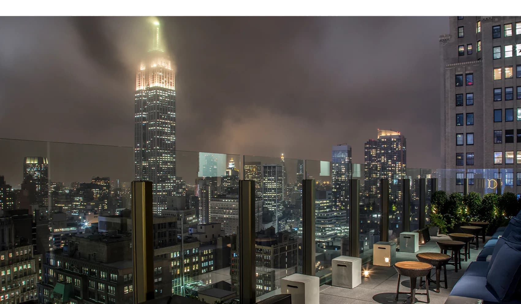 Nighttime cityscape rendering of Manhattan skyline with illuminated skyscrapers and rooftop terrace in foreground by McKay Architecture/Design.