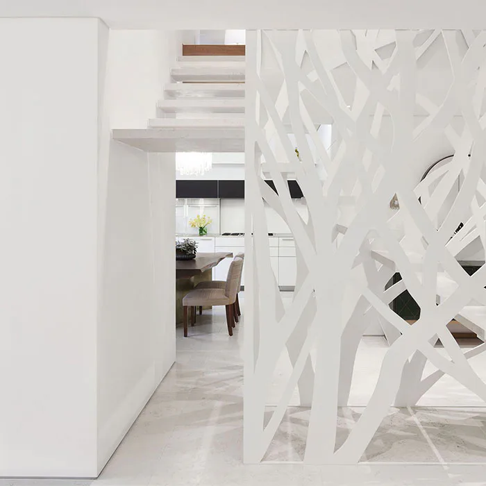 Modern white interior hallway with sculptural perforated room divider, leading to kitchen and dining area, minimalist palette by McKay Architecture/Design.