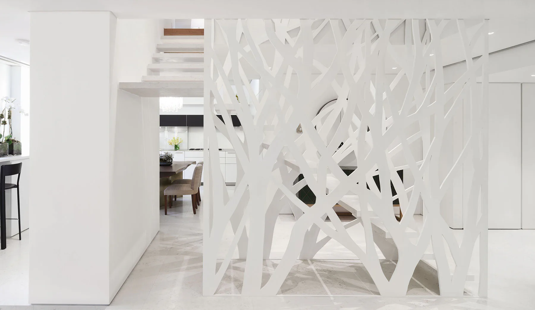 Minimalist white hallway with geometric perforated metal room divider creating intricate shadow patterns, designed by McKay Architecture/Design.