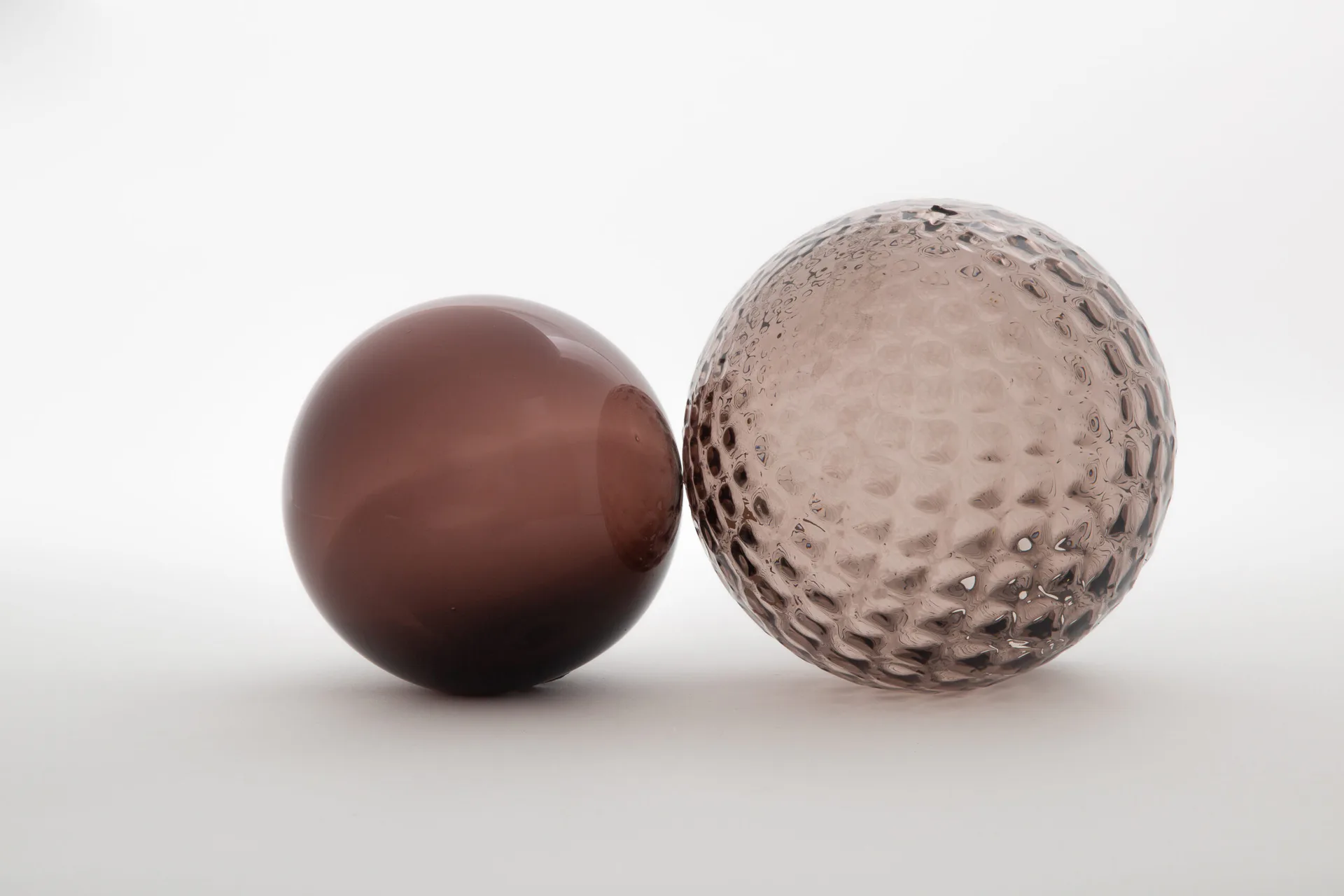Two spheres with contrasting surfaces—a smooth dark brown orb and a textured light gray dimpled sphere—rendered against a neutral gradient background by MDSG Studio.