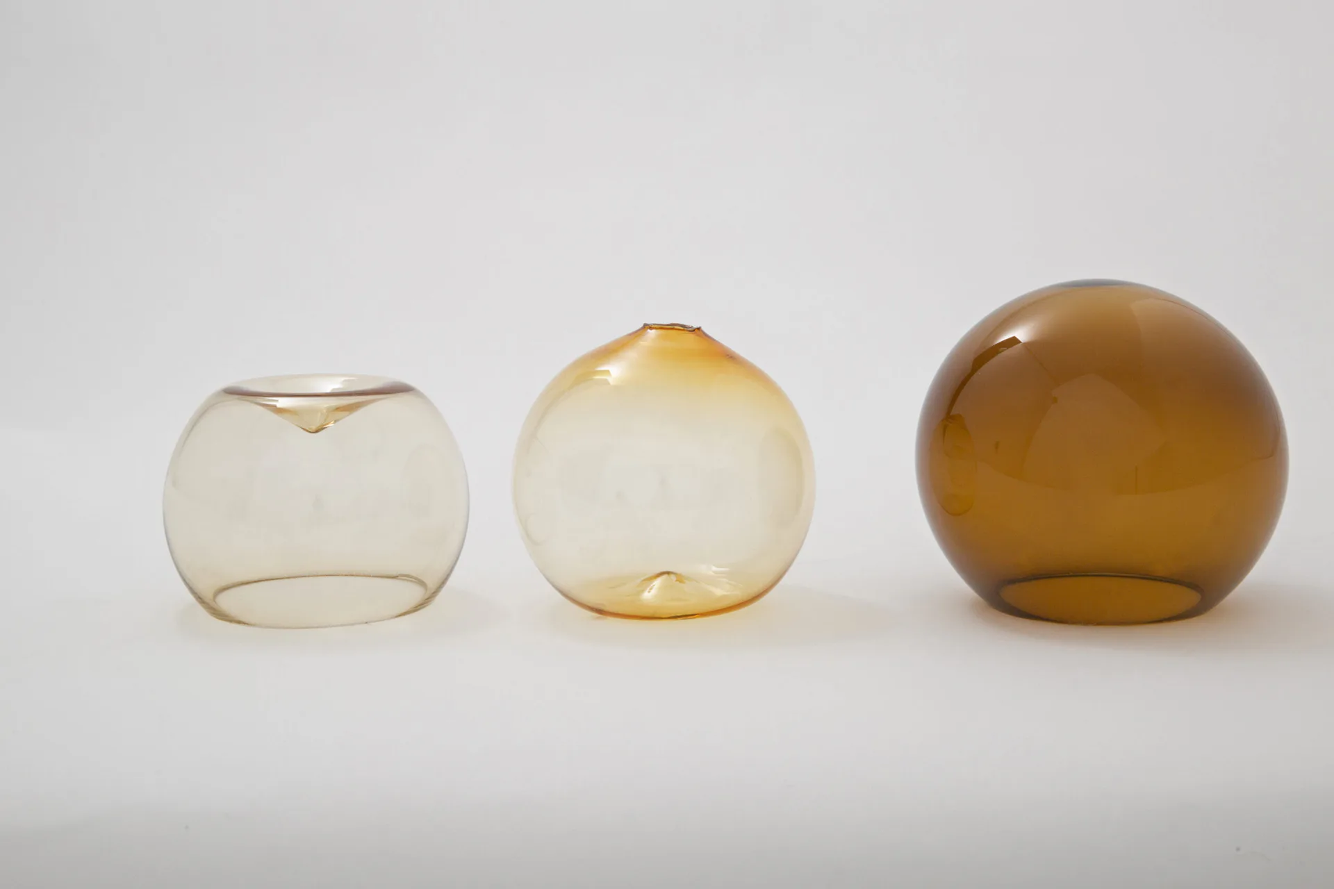Three translucent glass spheres in cream, pale yellow, and amber tones arranged on a white surface, showcasing material and form exploration by MDSG Studio.