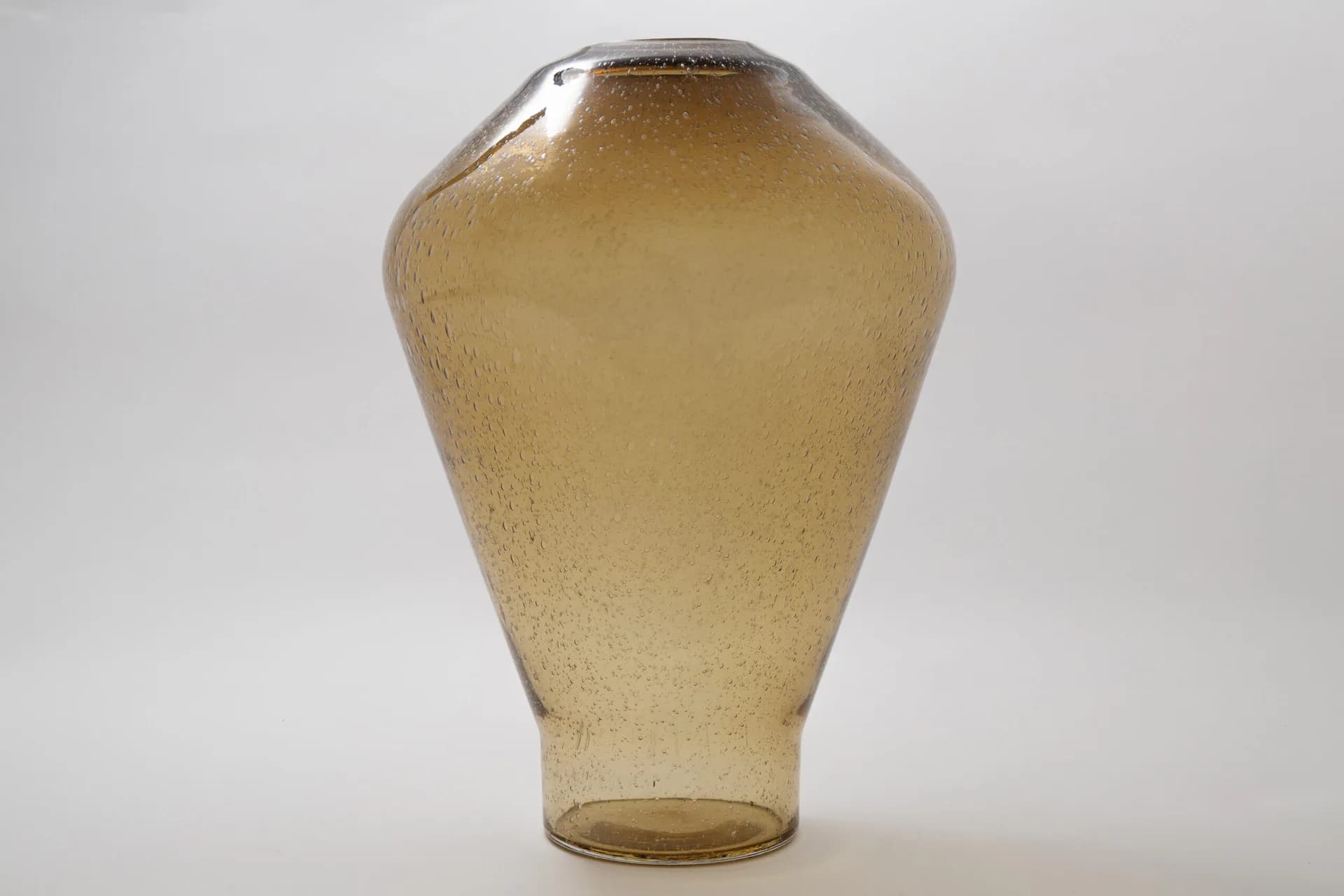 Amber glass vessel with organic bulbous form and tapered base, photographed against neutral background, by MDSG Studio.