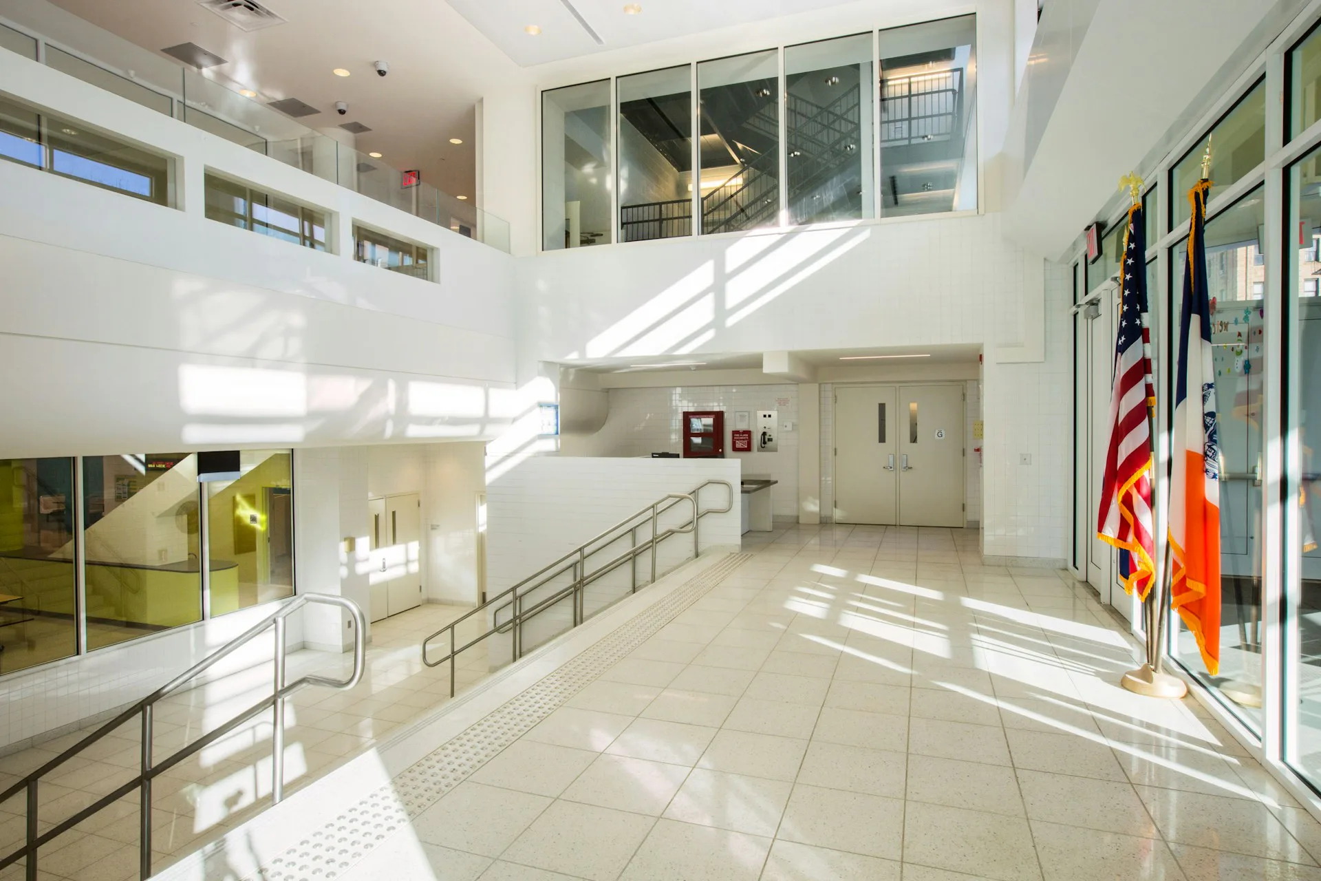 Bright, multi-level institutional interior with natural light, steel railings, tile flooring, and bulletin boards, designed by MDSzerbaty Associates Architecture LLC.