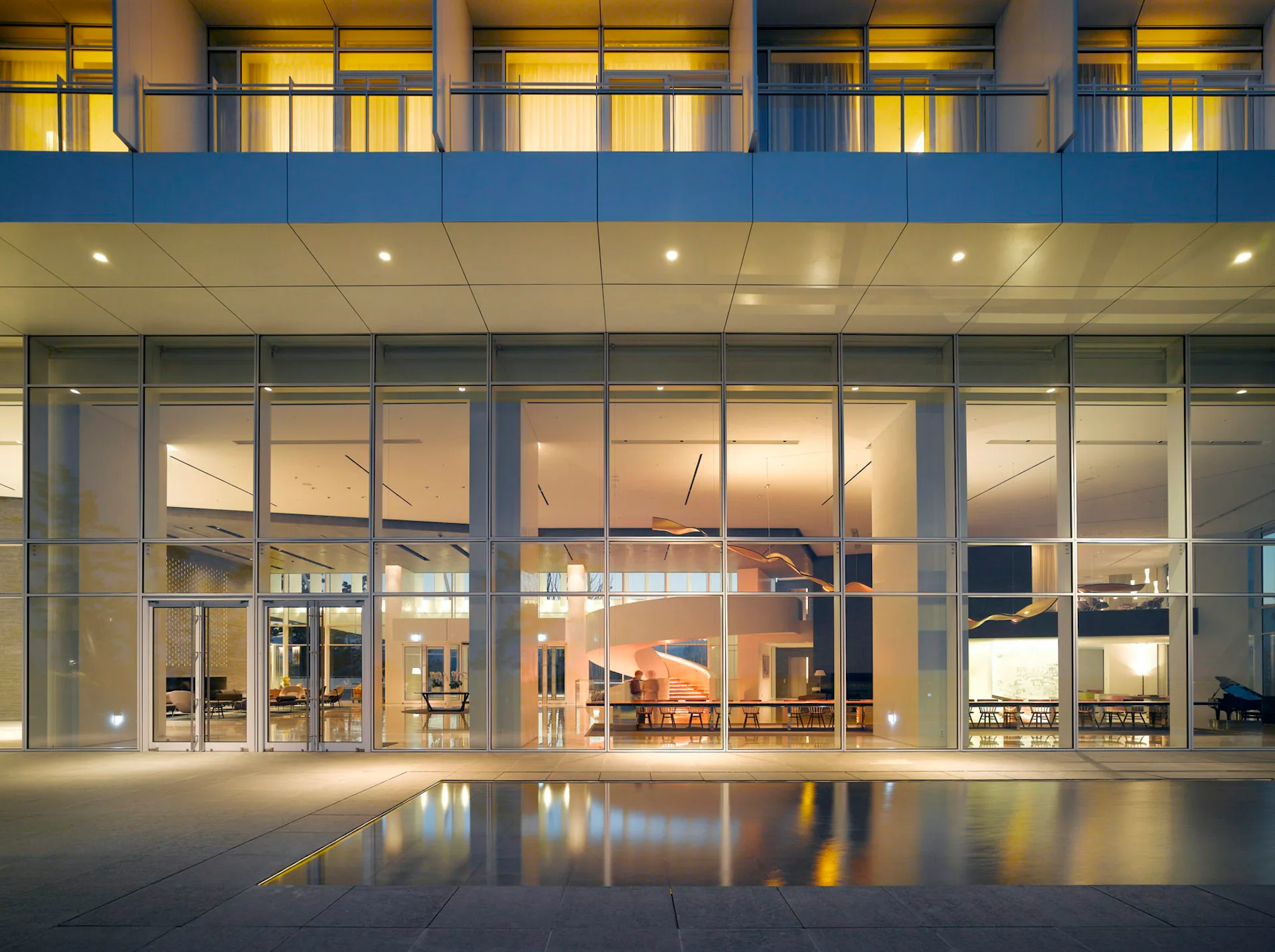 Modern glass-fronted lobby with warm wood interior, illuminated storefront at dusk by Meier Architects.